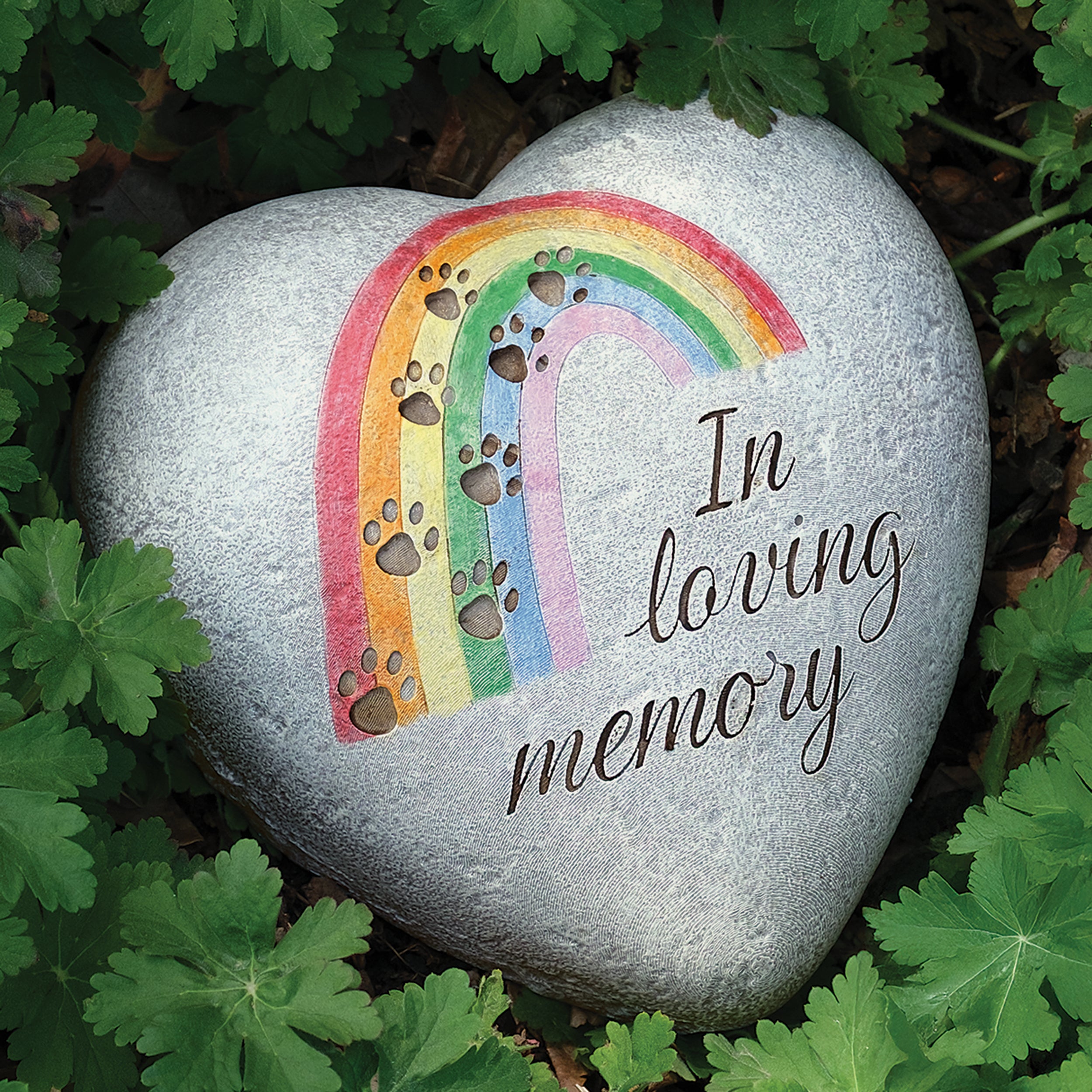 Heart shaped garden stone with rainbow and paw prints with "in loving memory" script on a bed of leaves