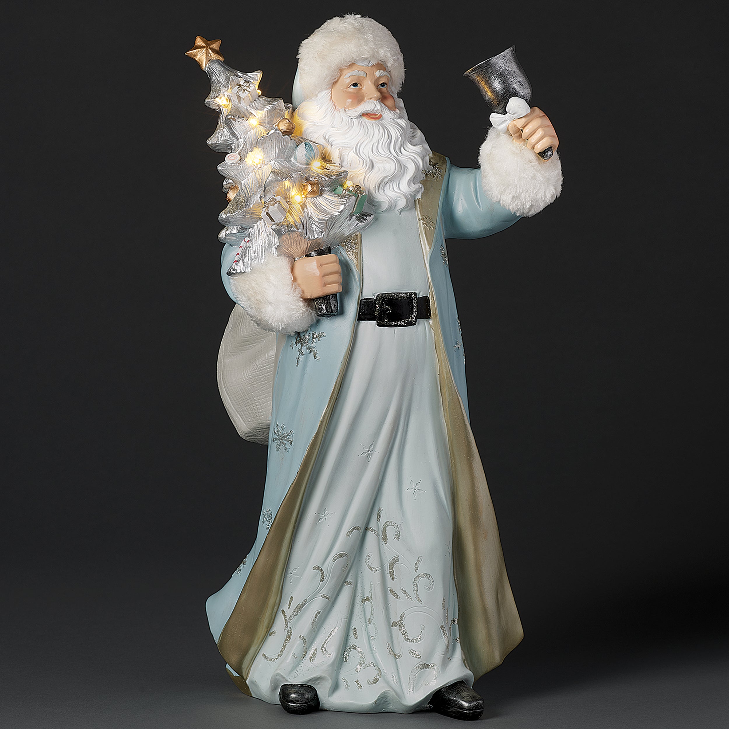 Decorative figure of Santa in a long blue coat holding a small tree and a lantern on a dark background