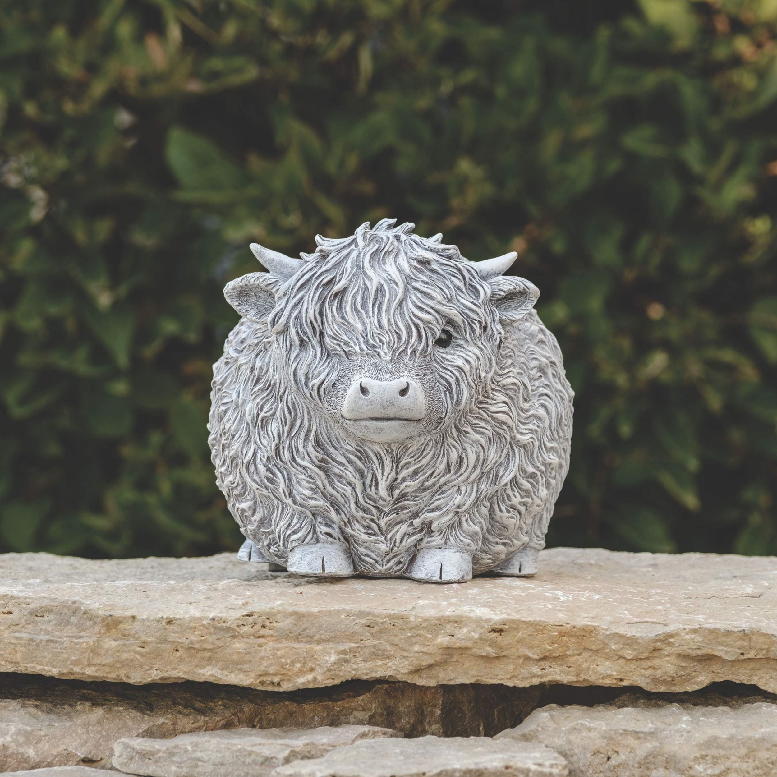 Statue of a fluffy highland cow on a rock with a blurred green background