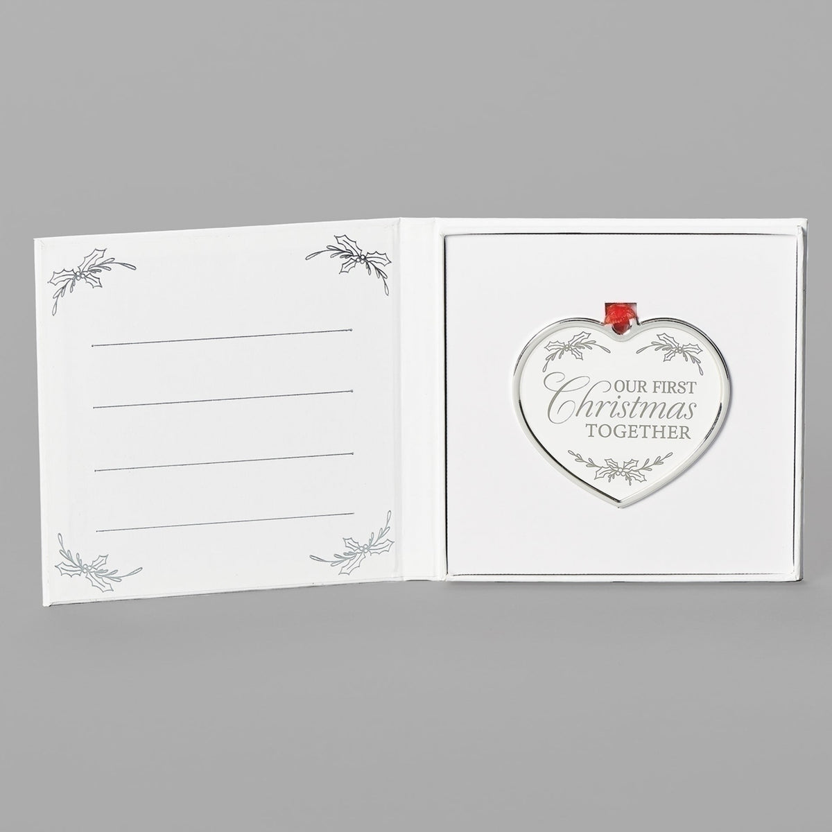 Open keepsake packaging showing the Our First Christmas heart ornament beside a printed message.
