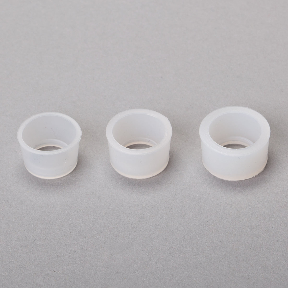 Three white ring-shaped candle accessories arranged in a row on a gray background.