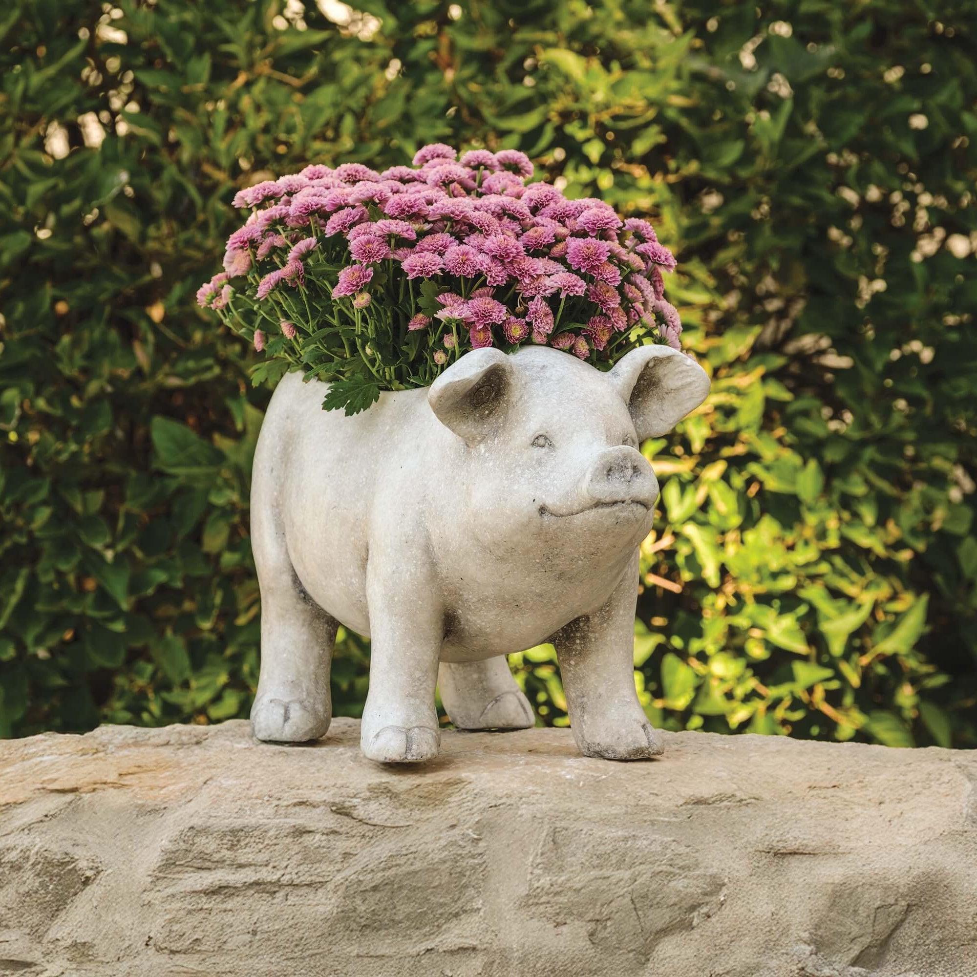 Pig-shaped planter with pink flowers on a stone surface with green foliage in the background
