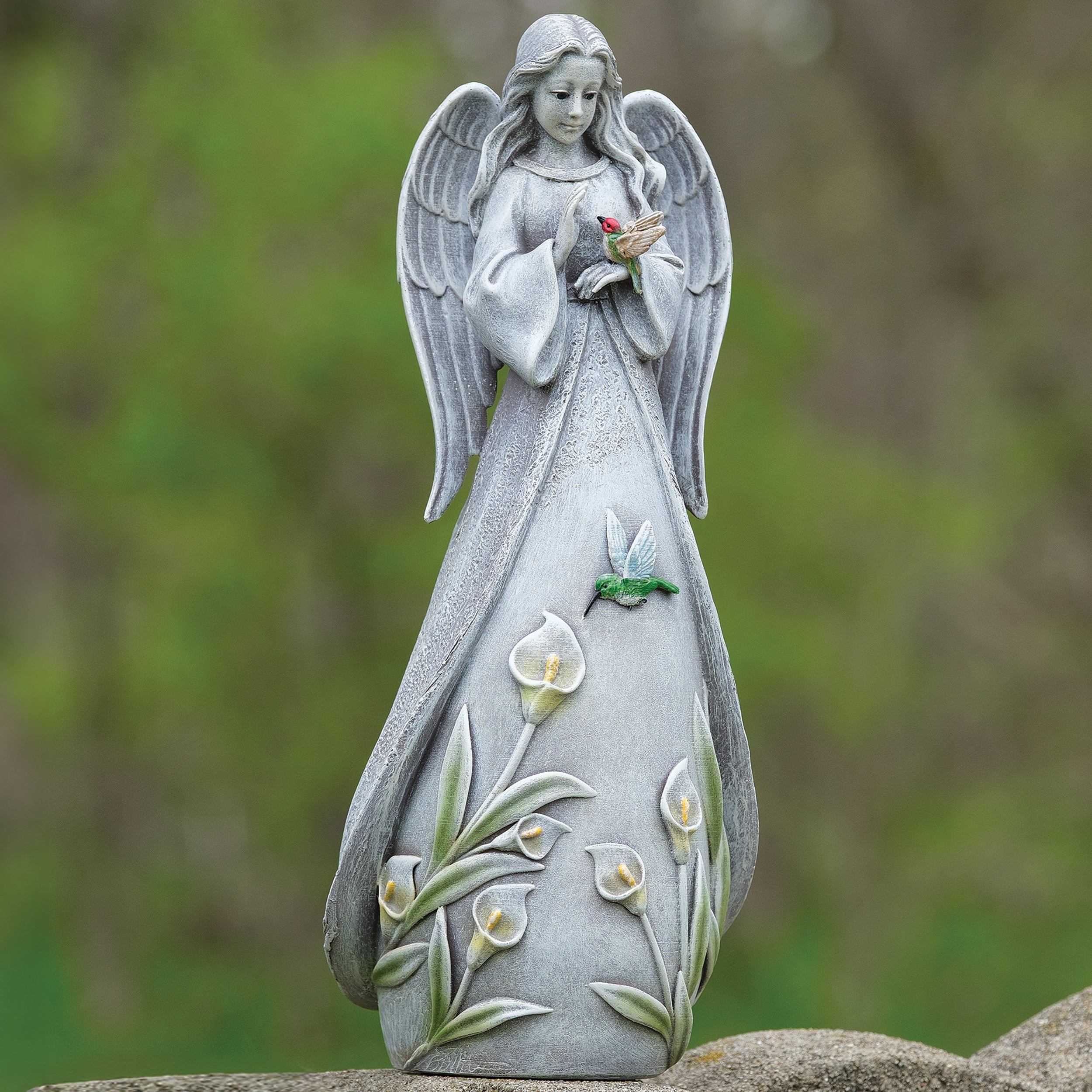 Statue of an angel holding a bird with floral designs on a natural background