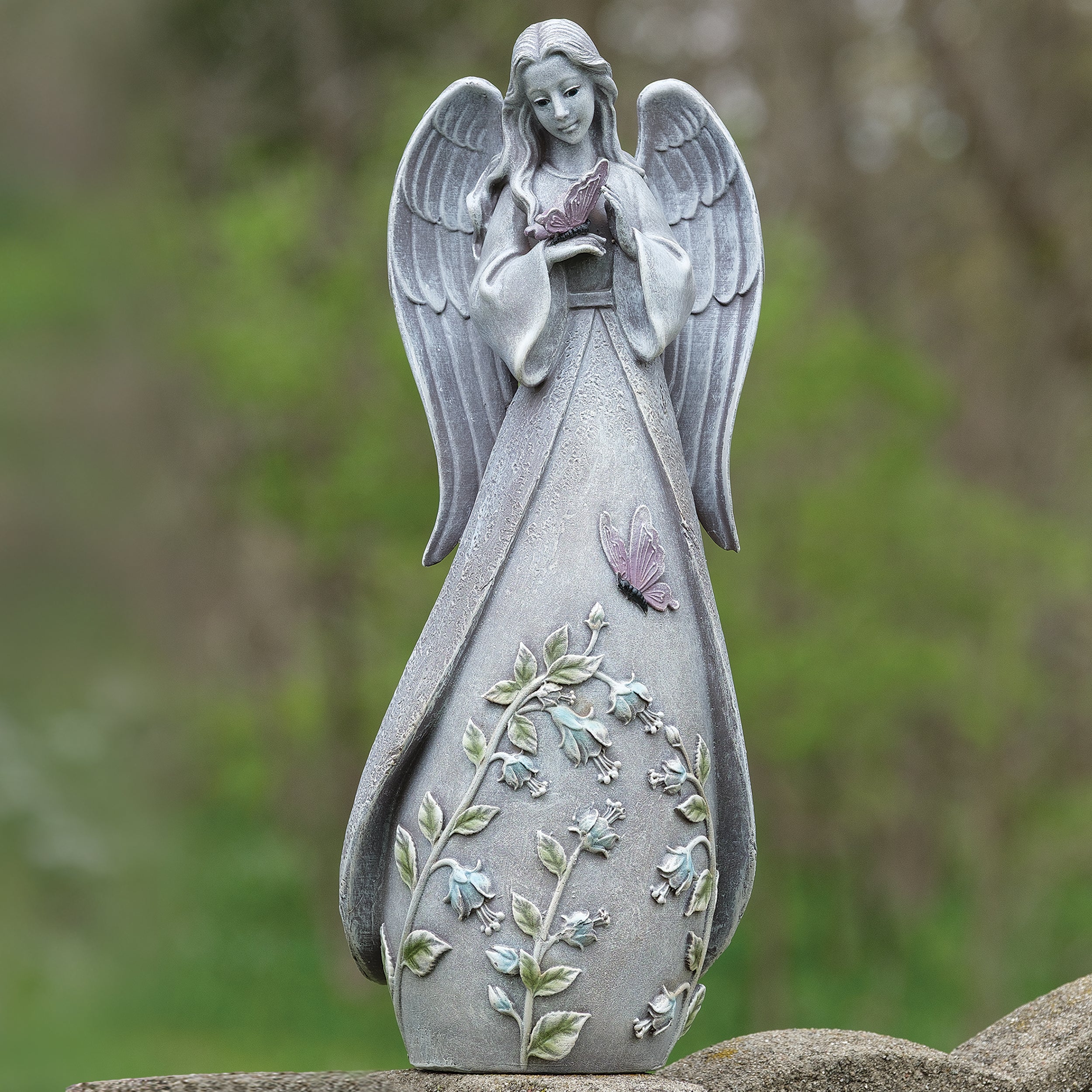 Statue of an angel with detailed wings and dress against a blurred natural background