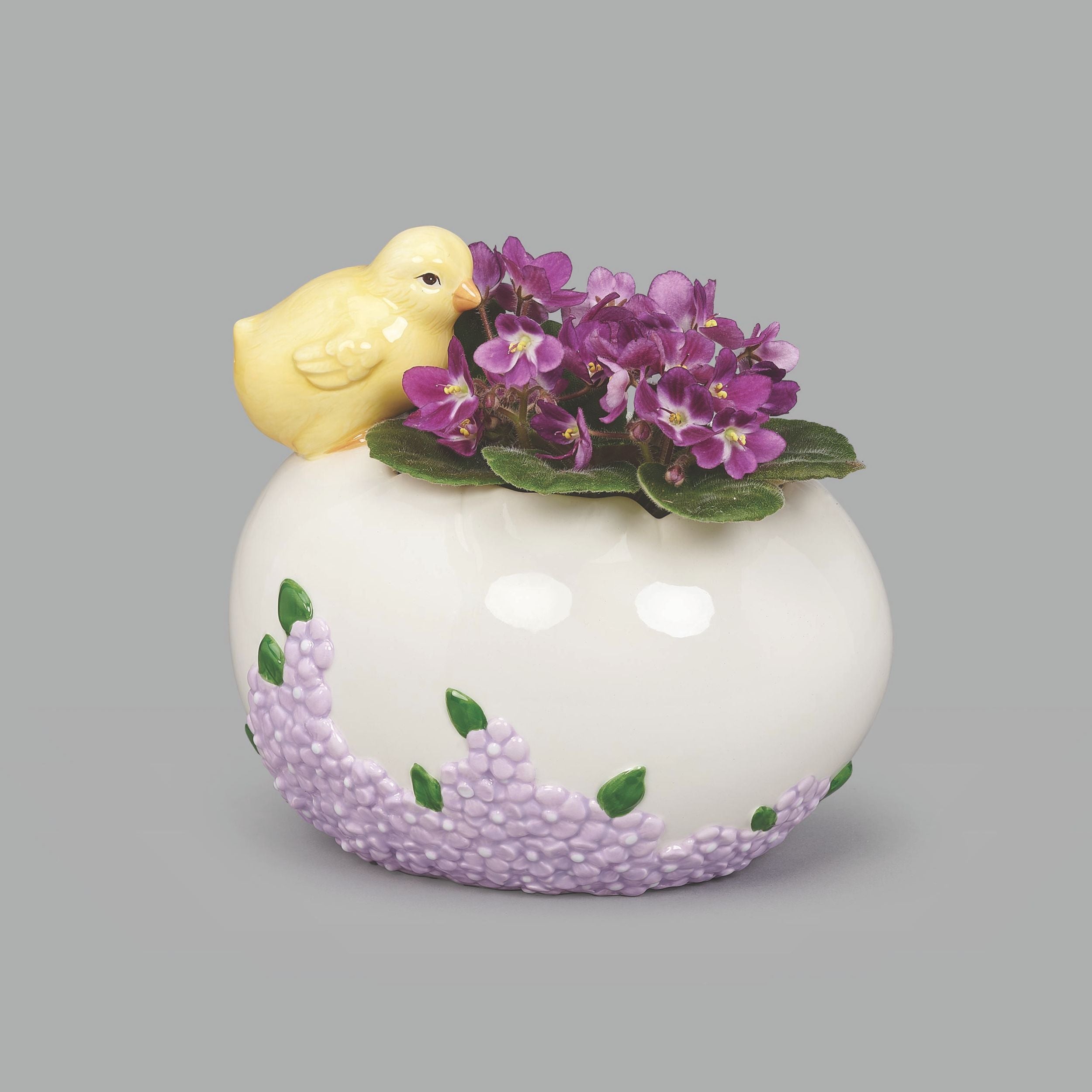 Decorative item with a small yellow chick on top of a white base with purple floral patterns, against a gray background.