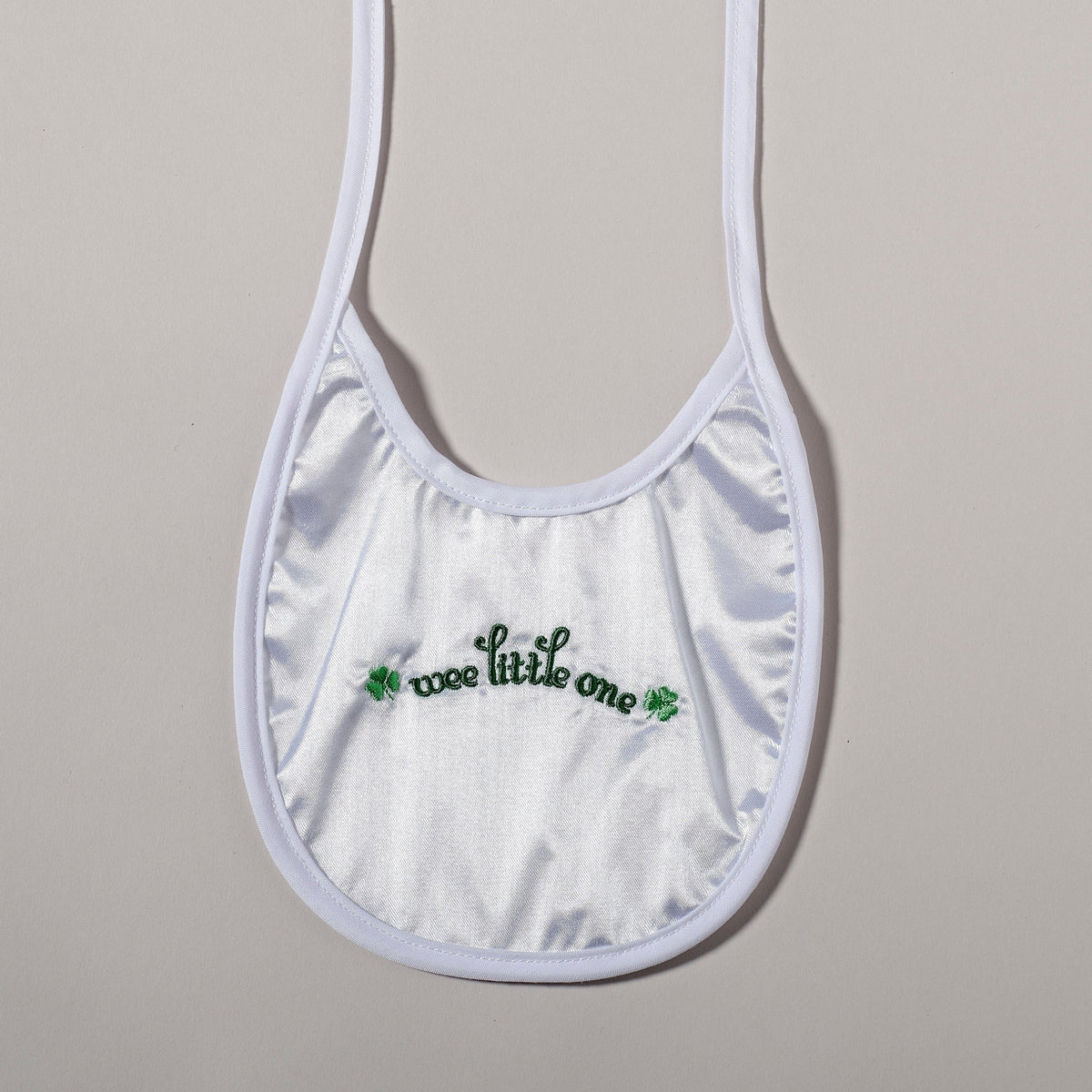 Front view of Irish baptism bib showing the green “wee little one” lettering, shamrock accents, and soft white fabric