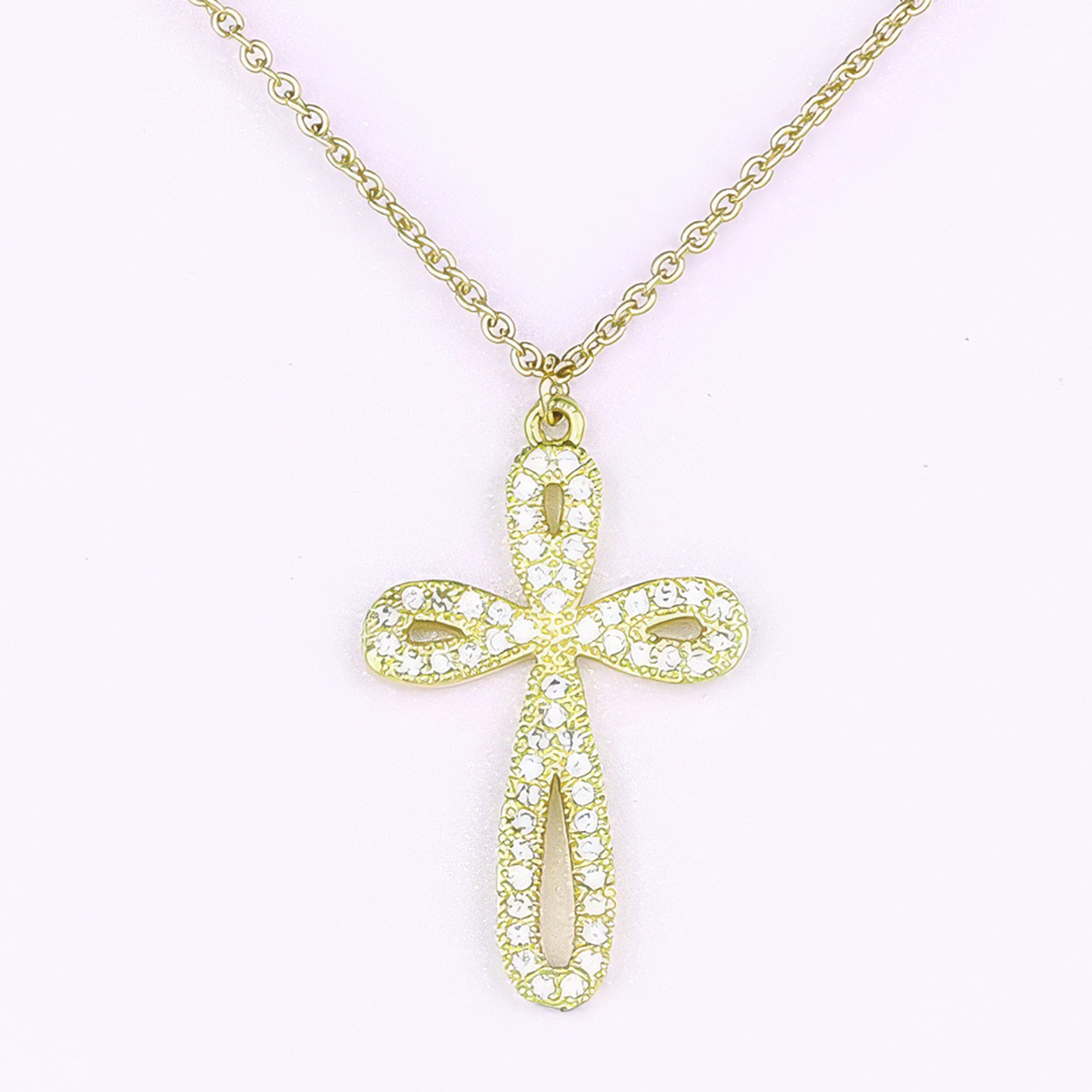 Gold cross necklace with clear stones on a light pink background