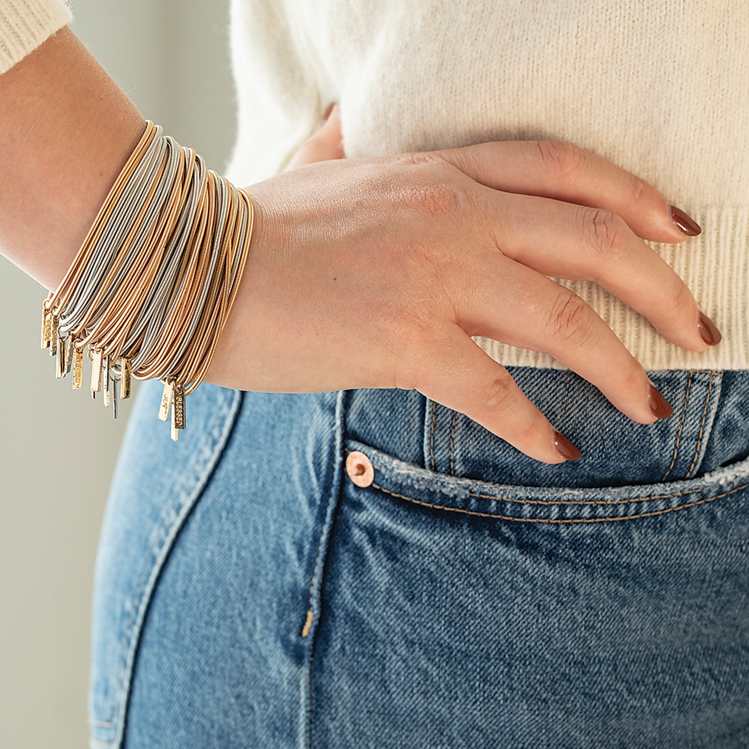 Person wearing multiple bracelets on a neutral background