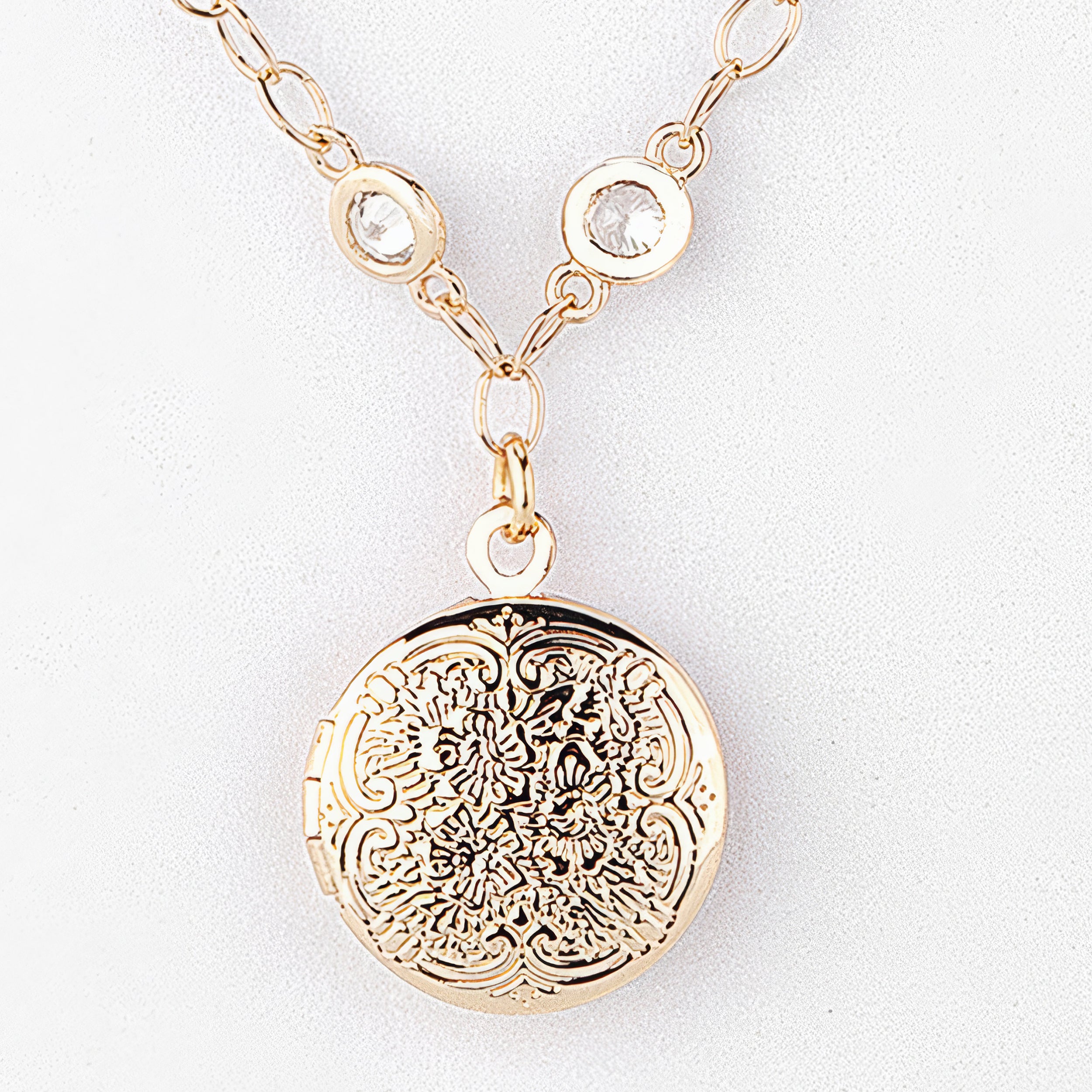 Gold necklace with a round, intricately designed pendant on a white background