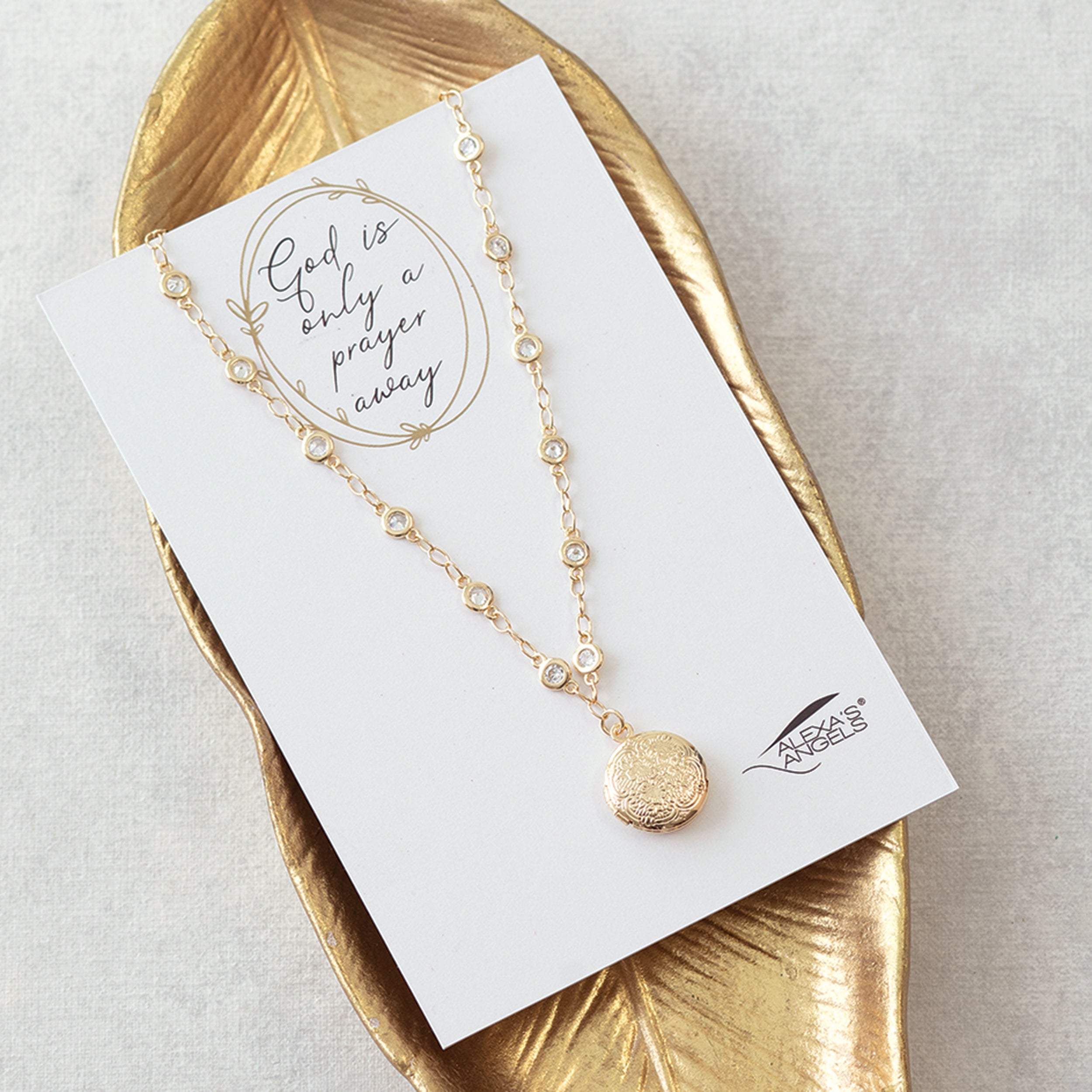 Gold necklace on a card with 'God is only a prayer away' text, displayed on a gold leaf