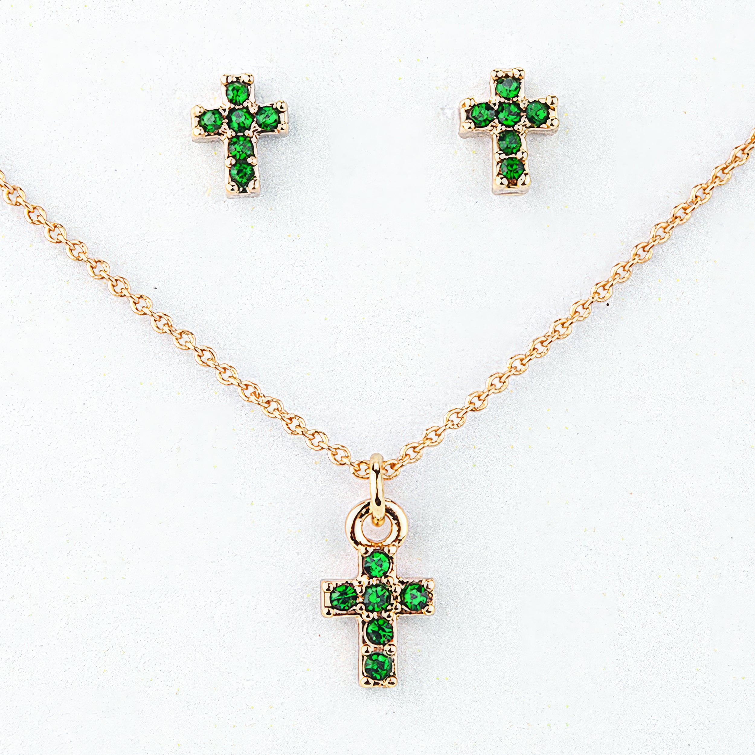 Gold cross necklace and earrings with green gemstones on a white background