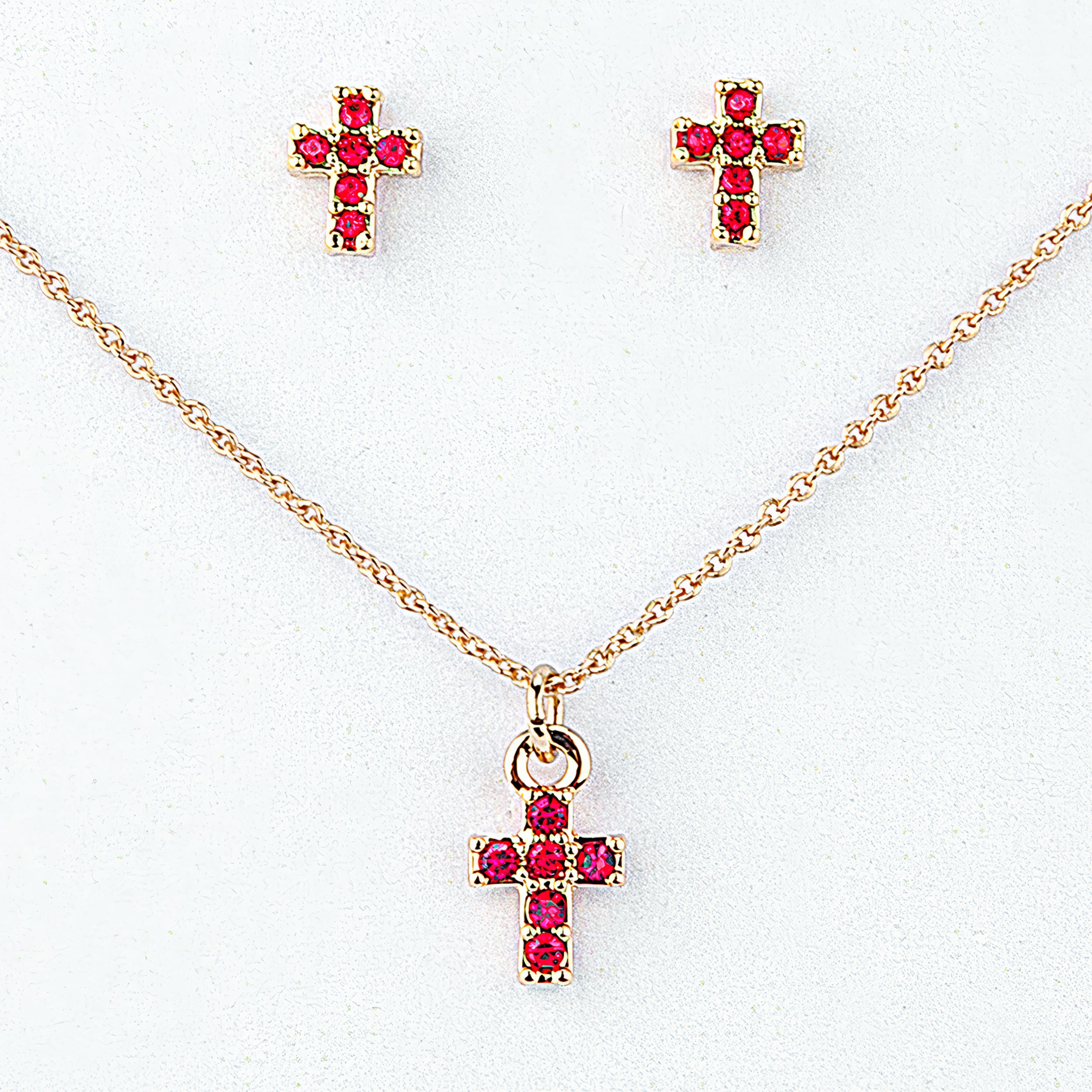Gold cross necklace and earrings with red gemstones on a white background