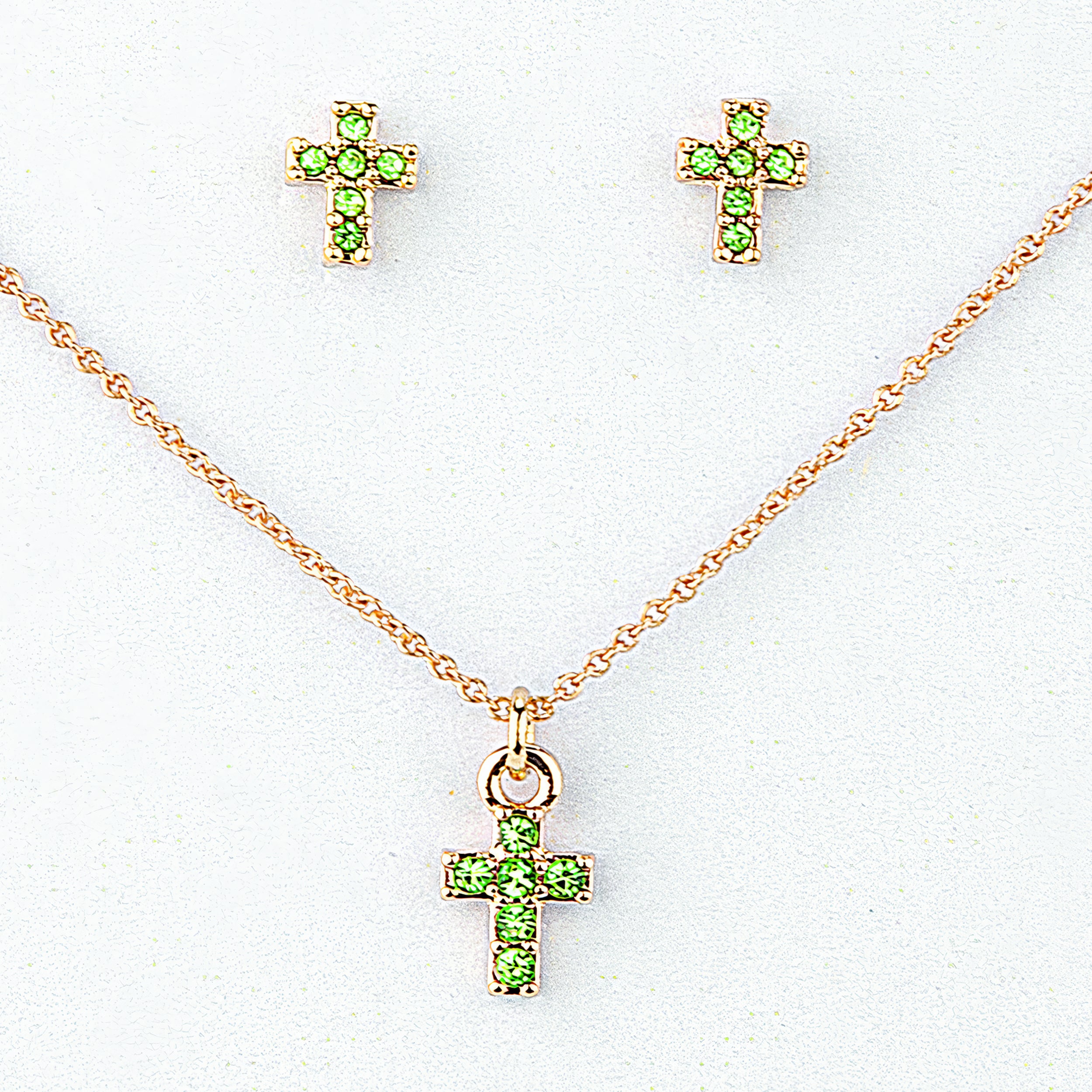 Gold cross necklace and earrings with green gemstones on a white background