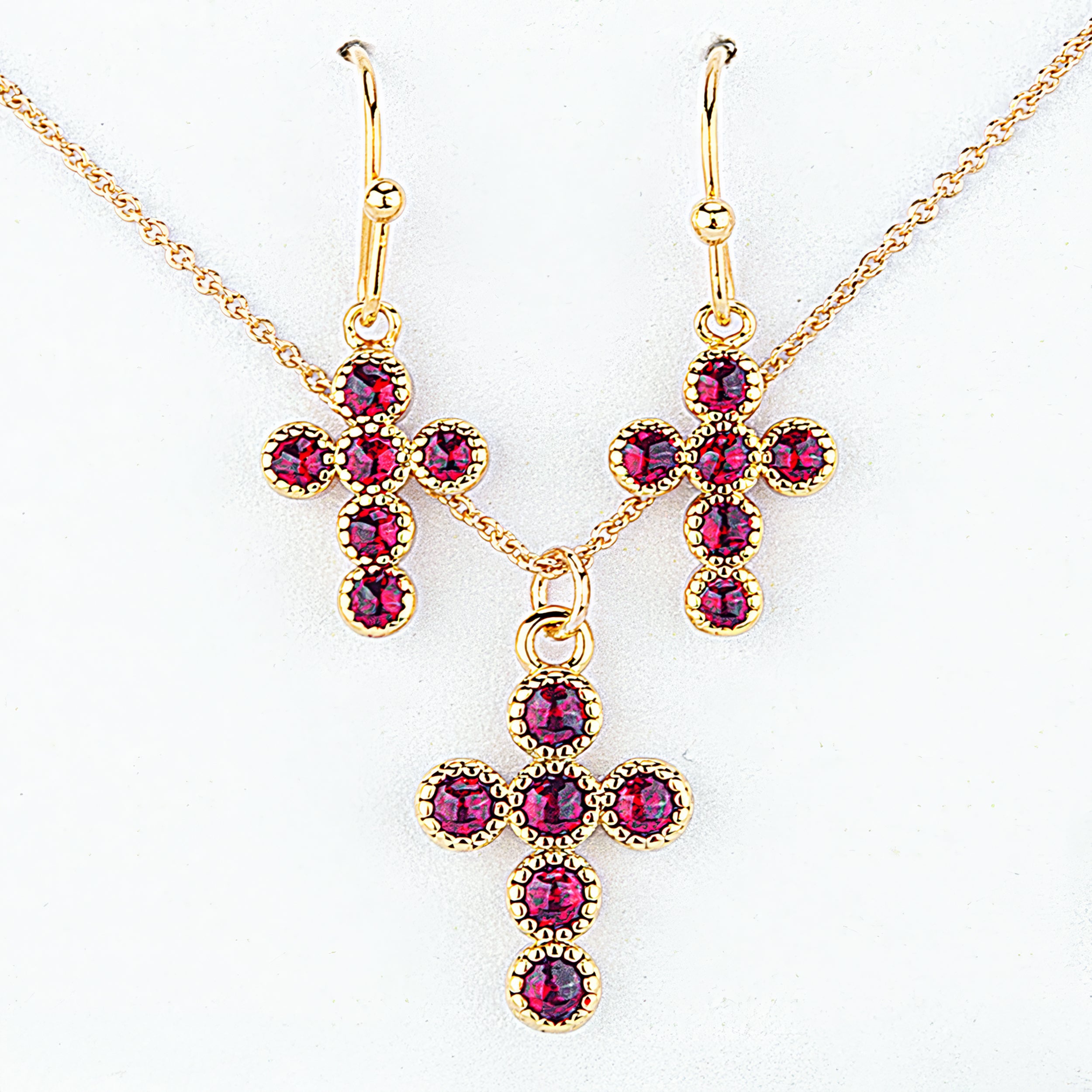 Gold cross-shaped jewelry set with red gemstones on a white background
