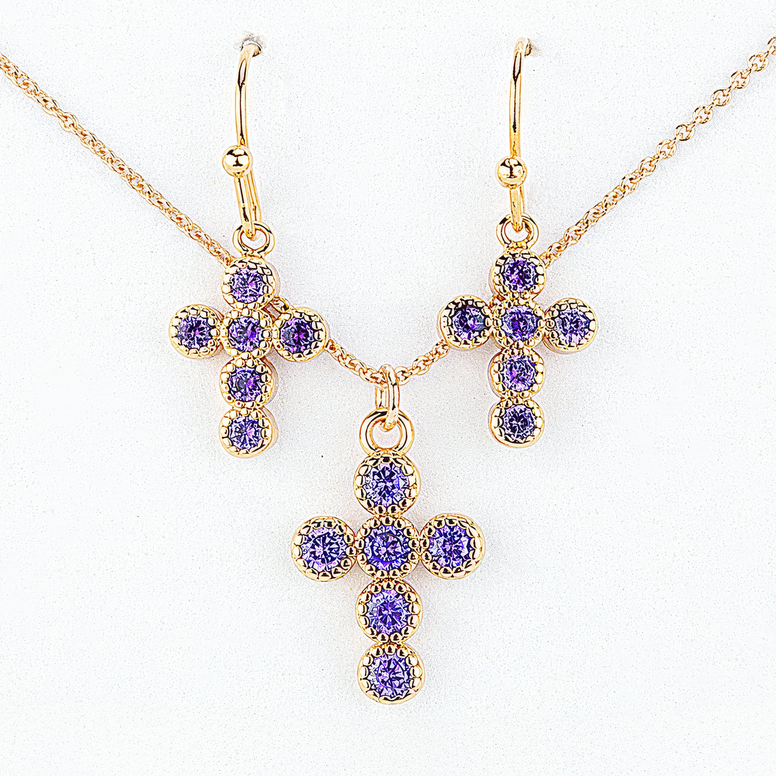 Gold cross-shaped jewelry set with purple gemstones on a white background