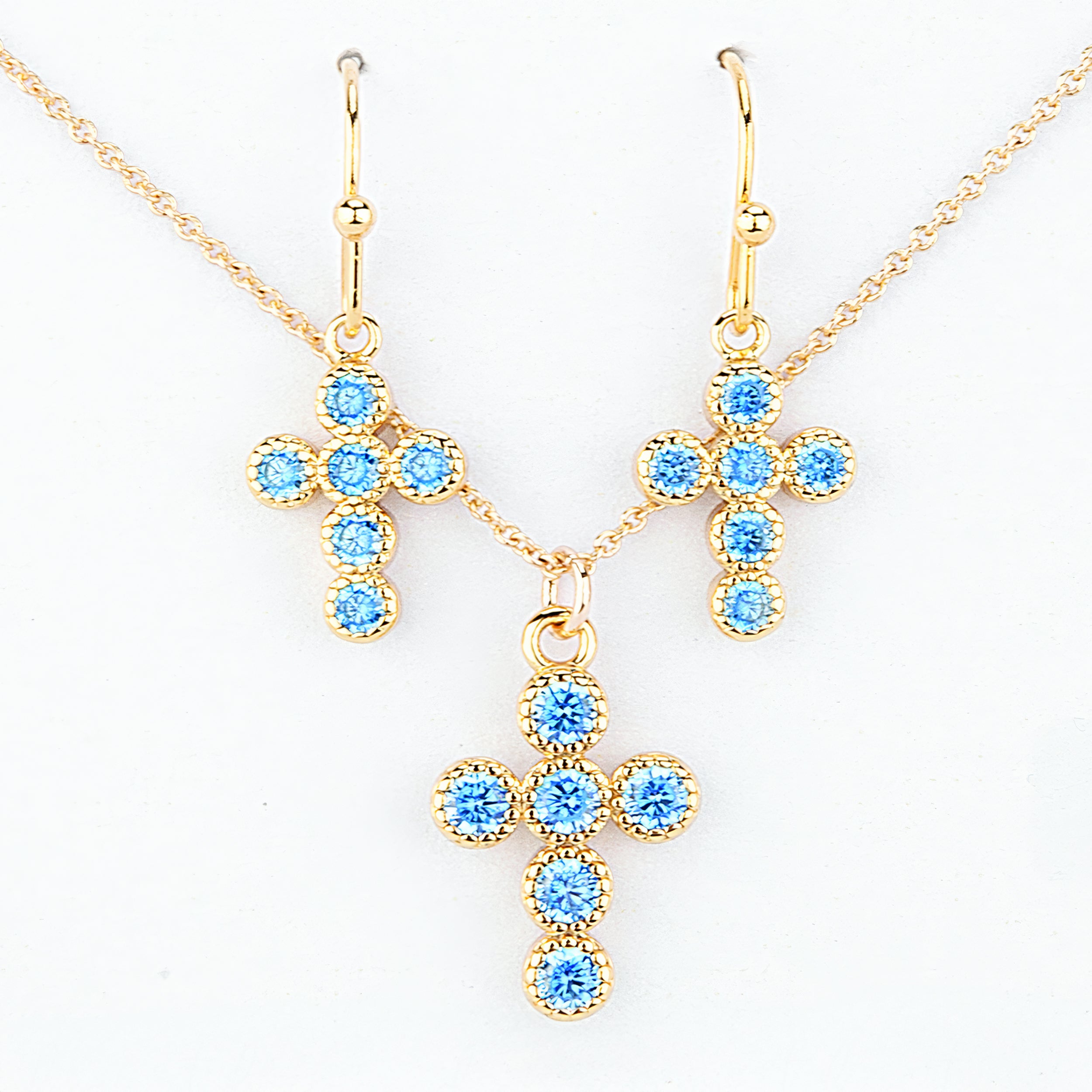 Gold cross-shaped jewelry set with blue gemstones on a white background