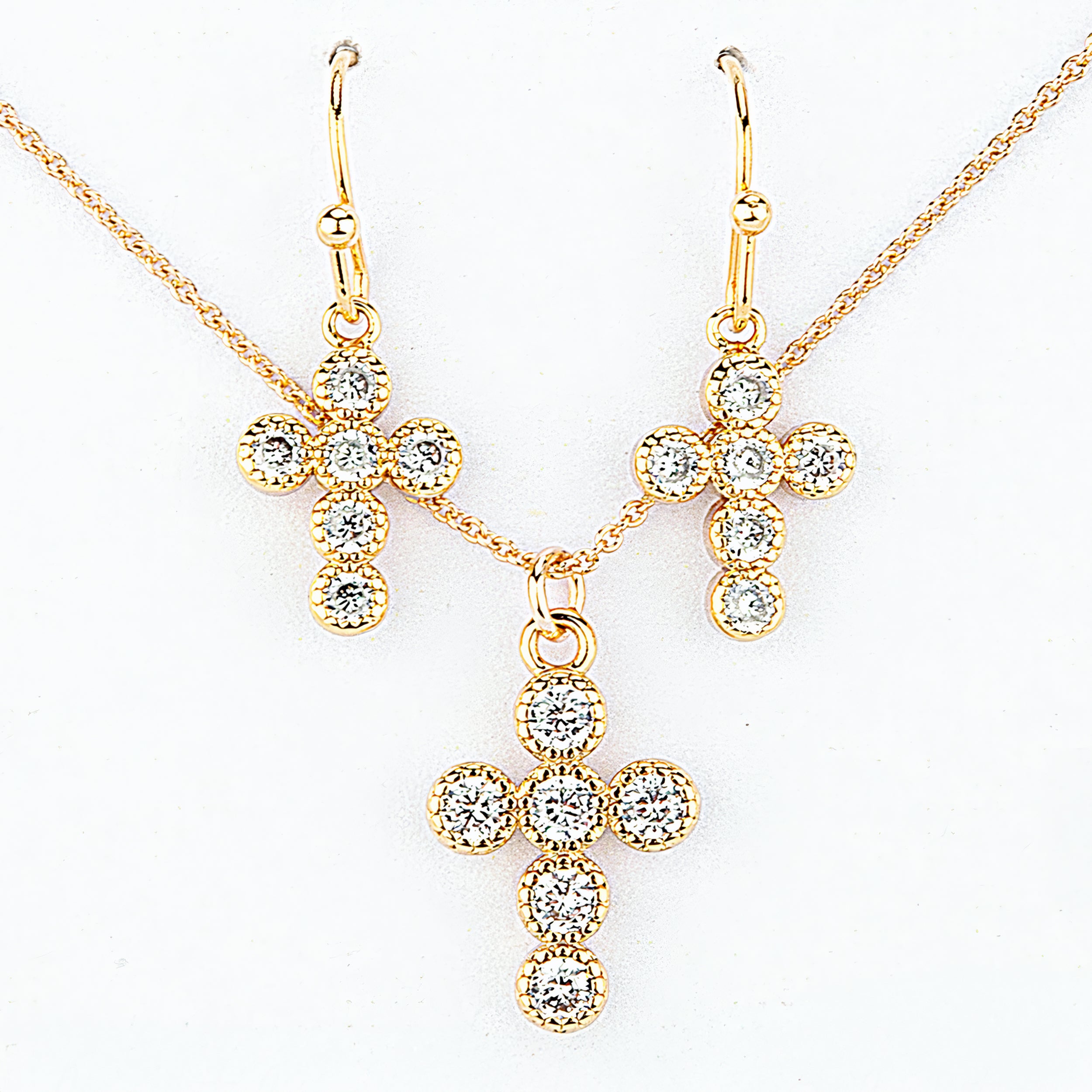 Gold cross necklace and earrings with clear gemstones on a white background