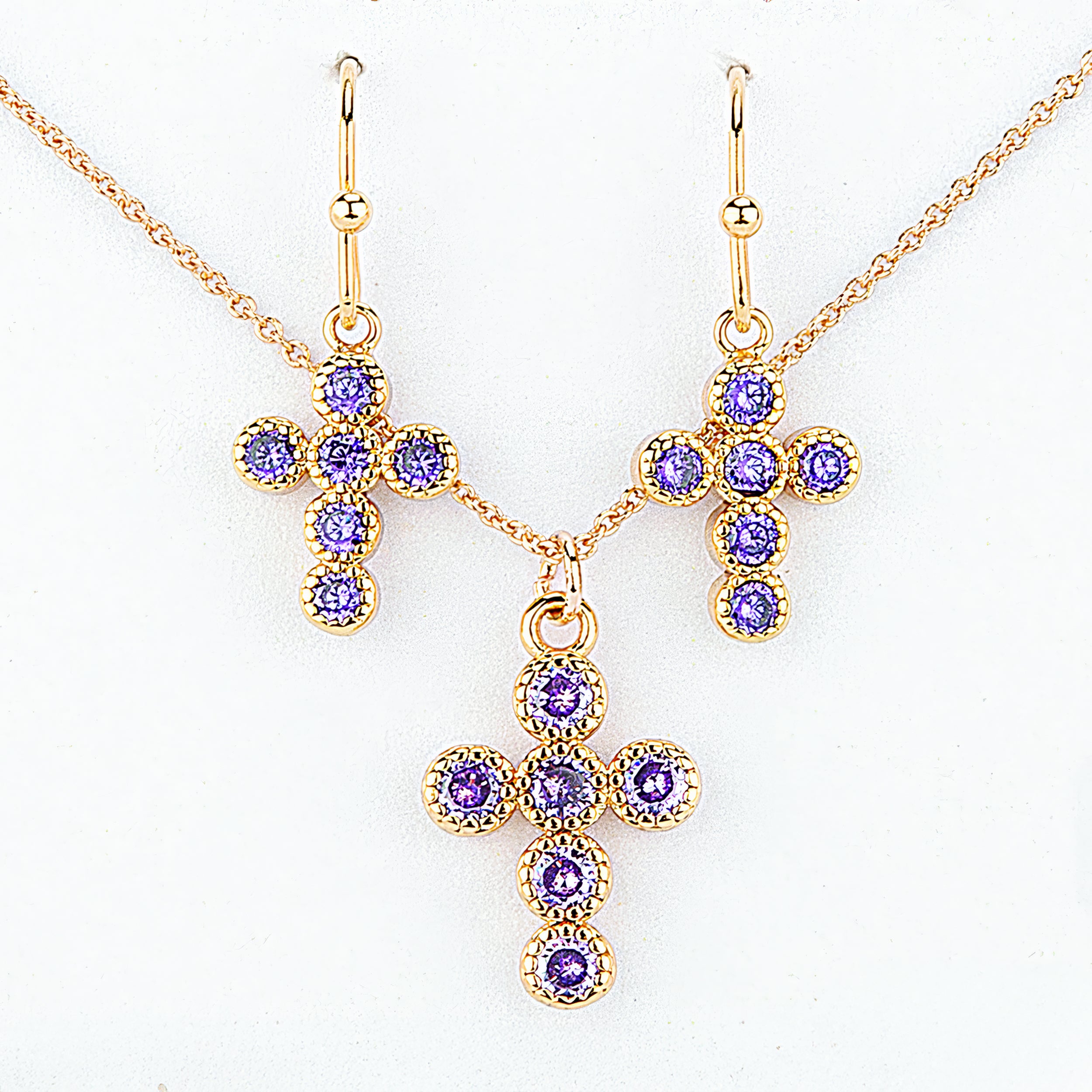 Gold cross necklace and earrings with purple gemstones on a white background