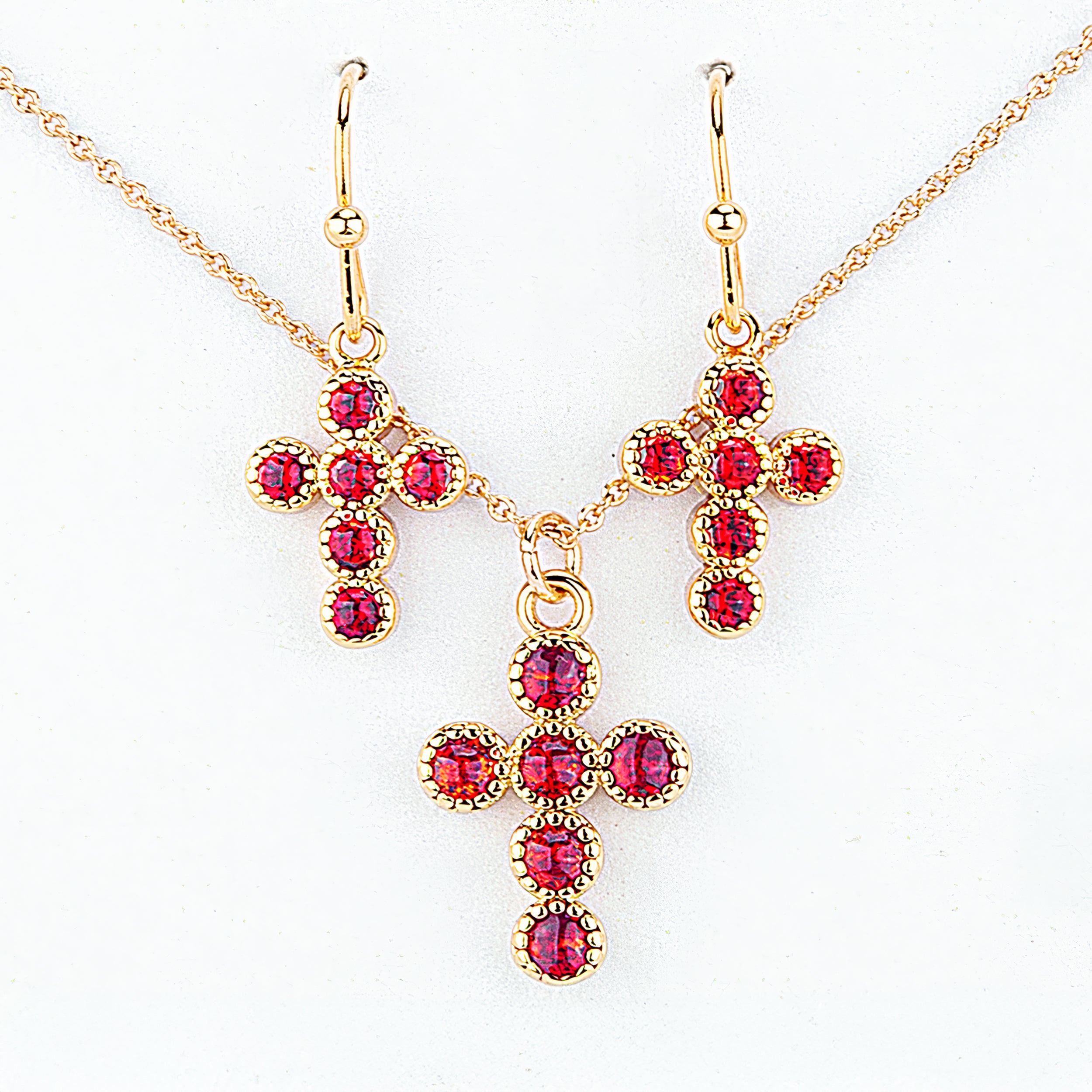 Gold cross-shaped jewelry set with red gemstones on a white background