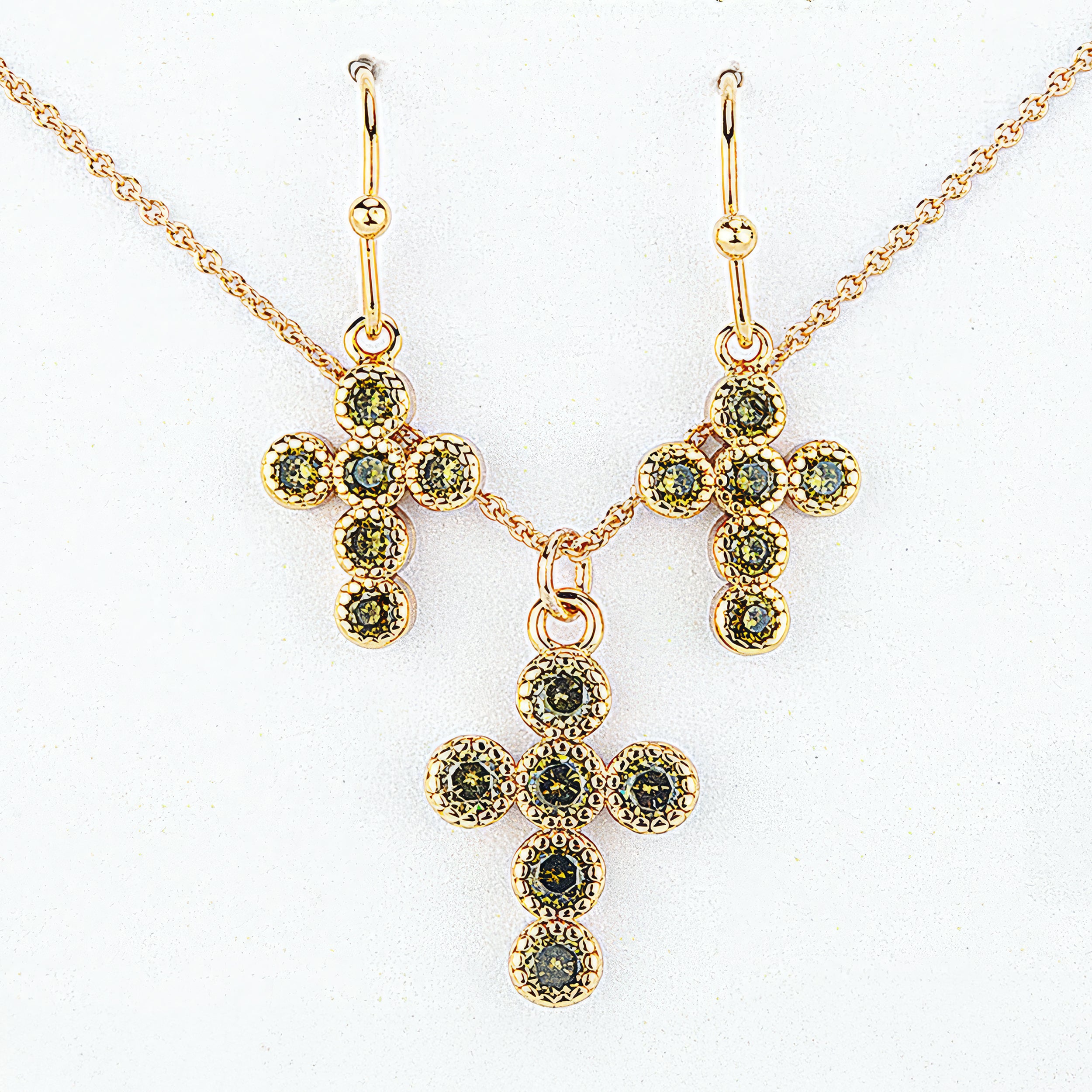 Gold cross-shaped jewelry set with green gemstones on a white background