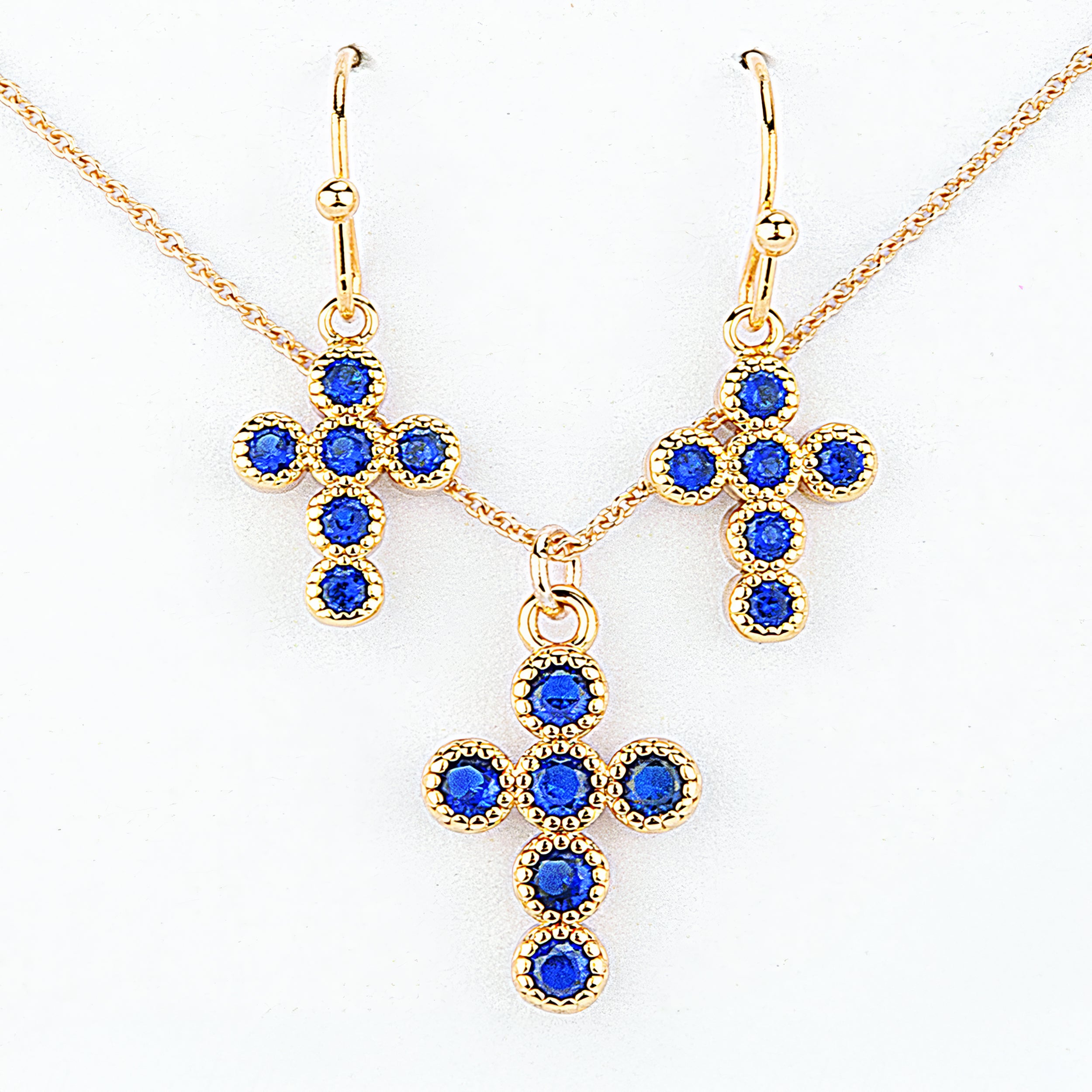 Gold cross-shaped jewelry set with blue stones on a white background