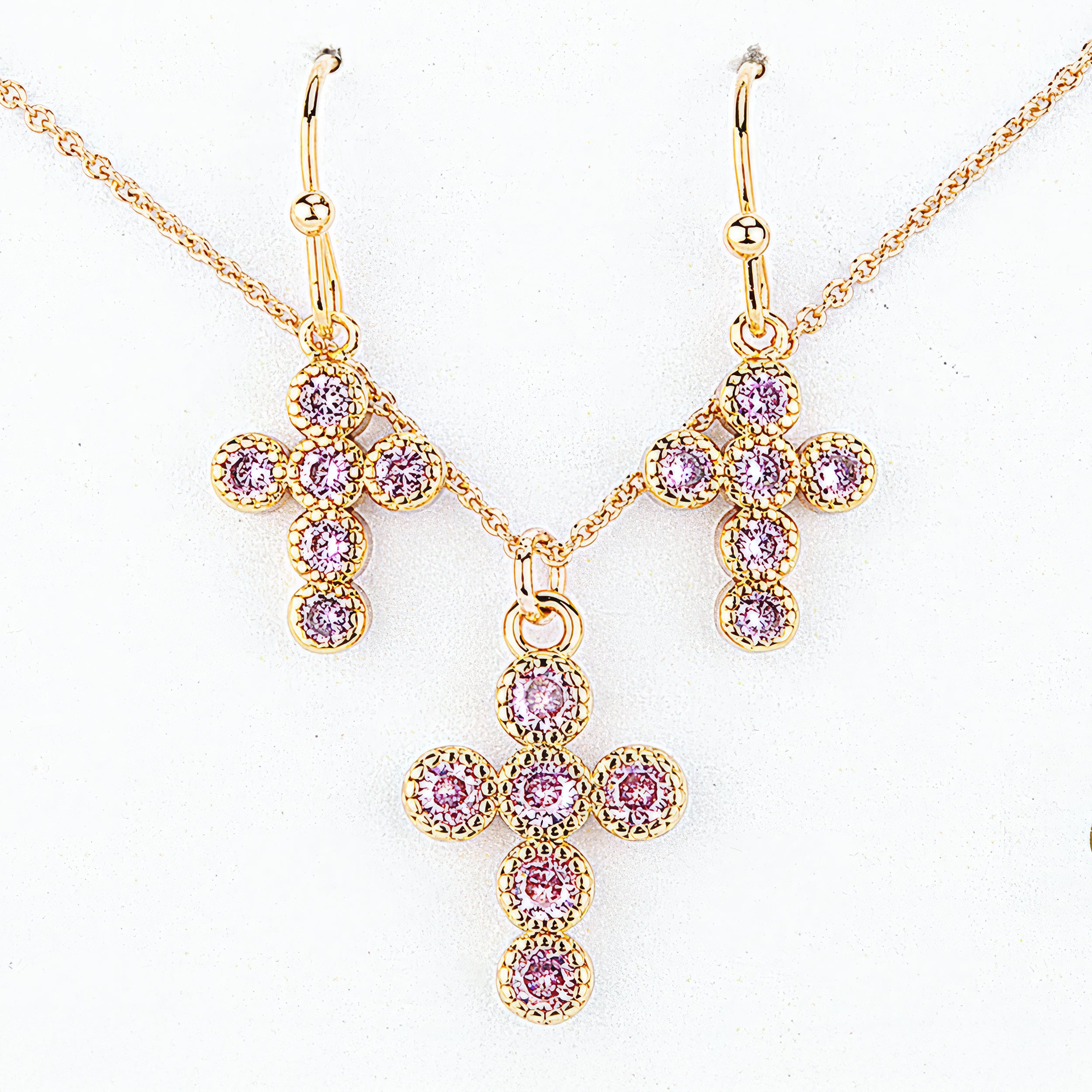 Gold cross necklace and earrings with pink gemstones on a white background
