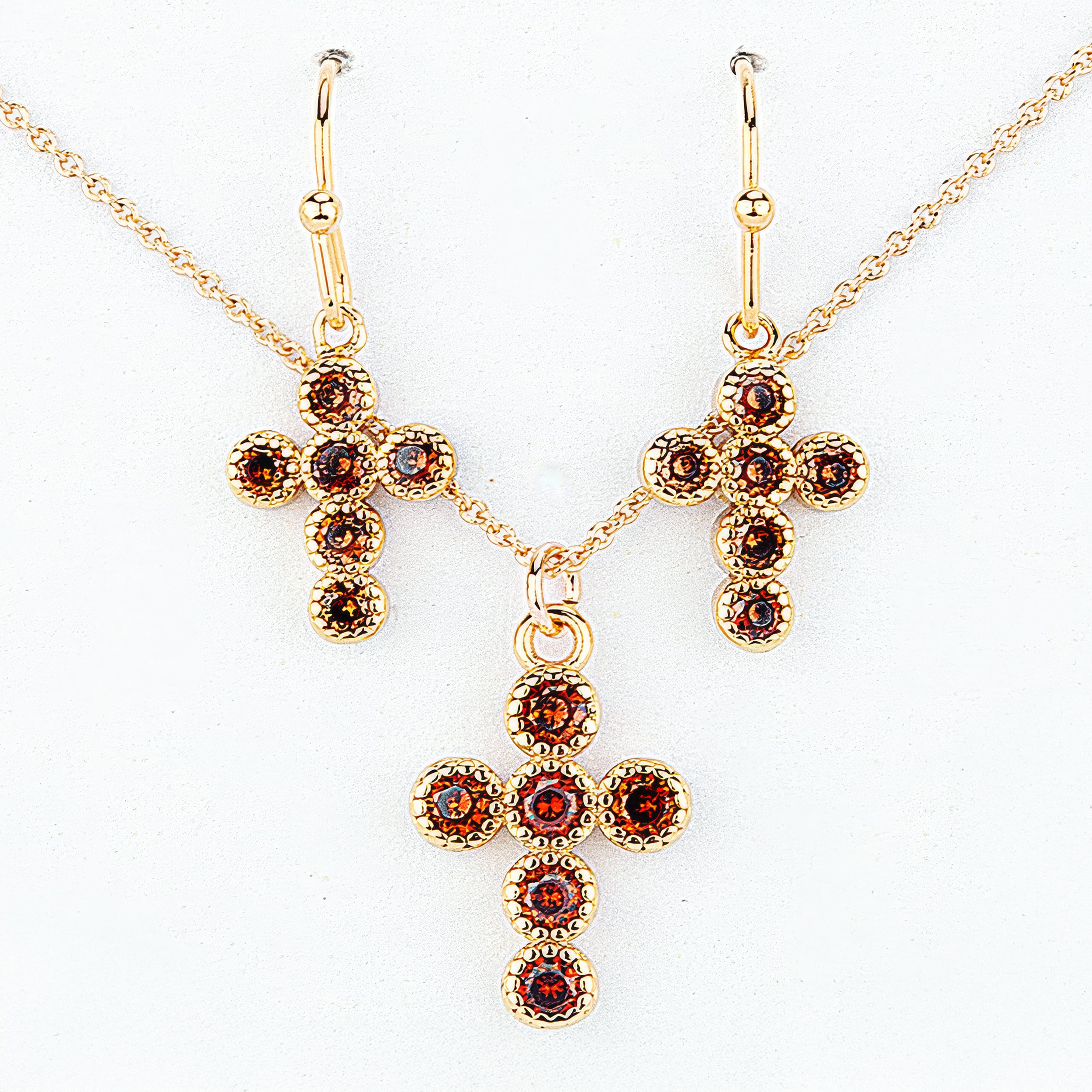 Gold cross necklace and earrings with red gemstones on a white background