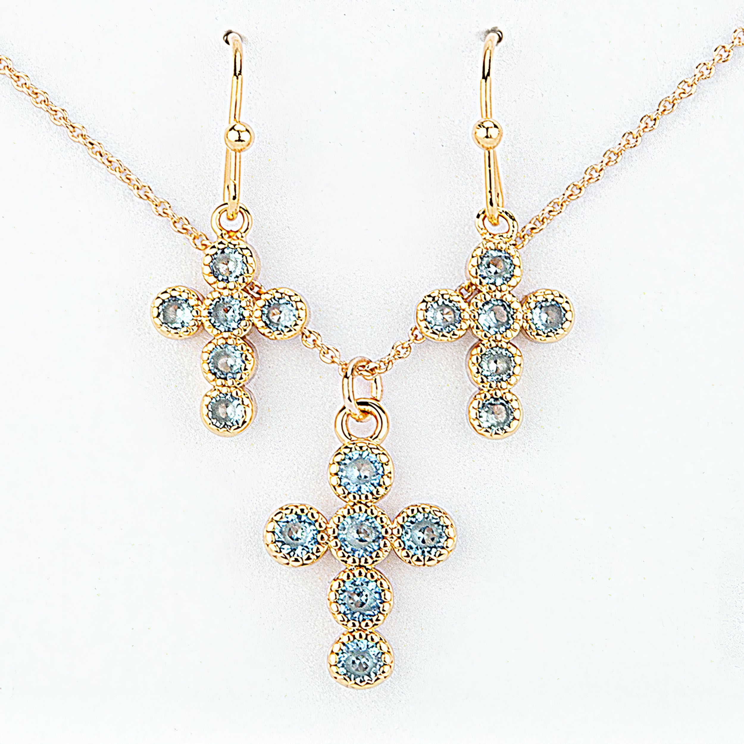 Gold cross-shaped necklace and earrings with blue gemstones on a white background