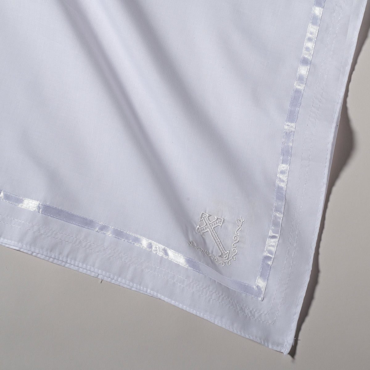 Close-up of White Baptism Blanket showing the smooth white fabric, satin-trimmed edge, and delicate embroidered detailing