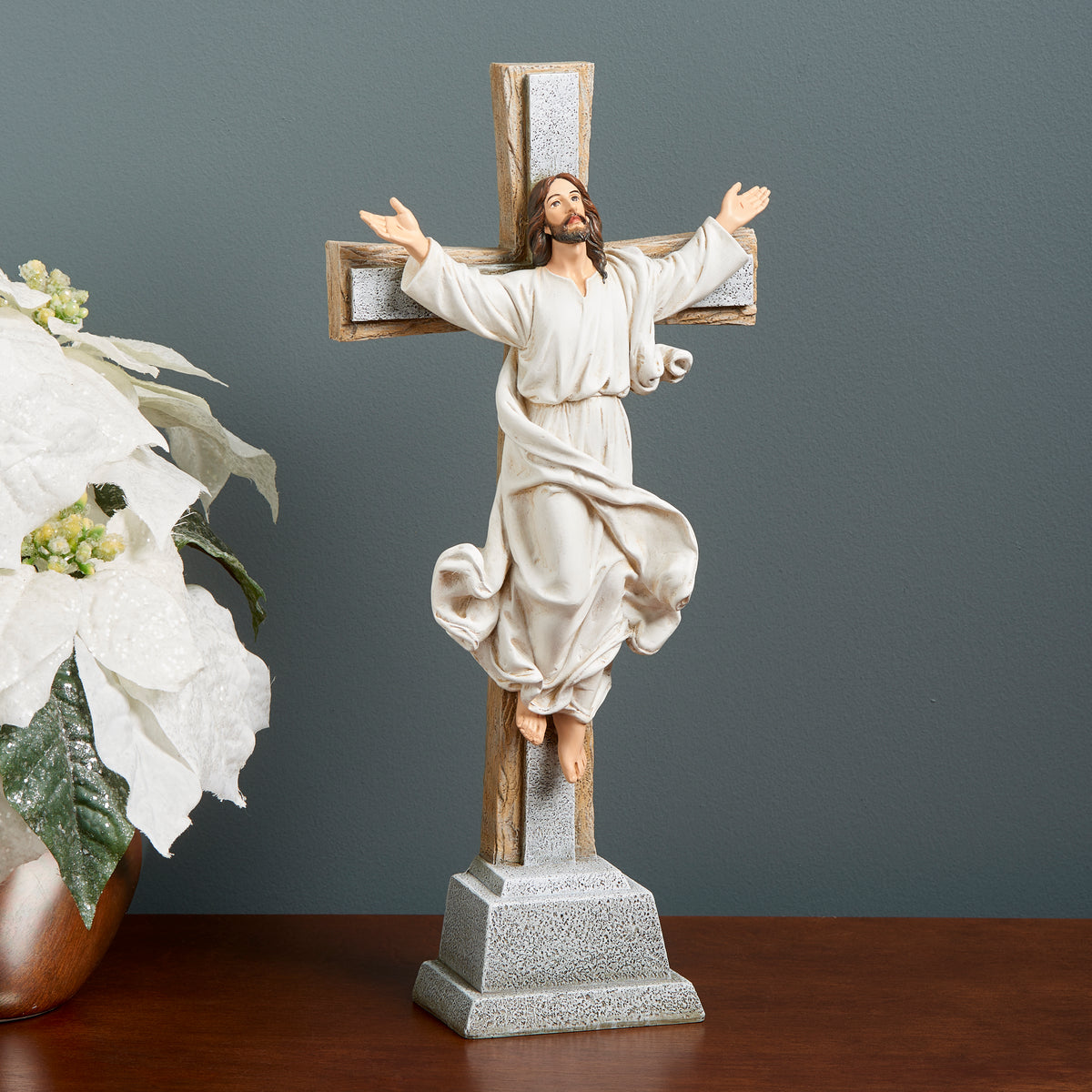 Joseph's Studio Risen Christ Standing Cross displayed on a tabletop beside white flowers