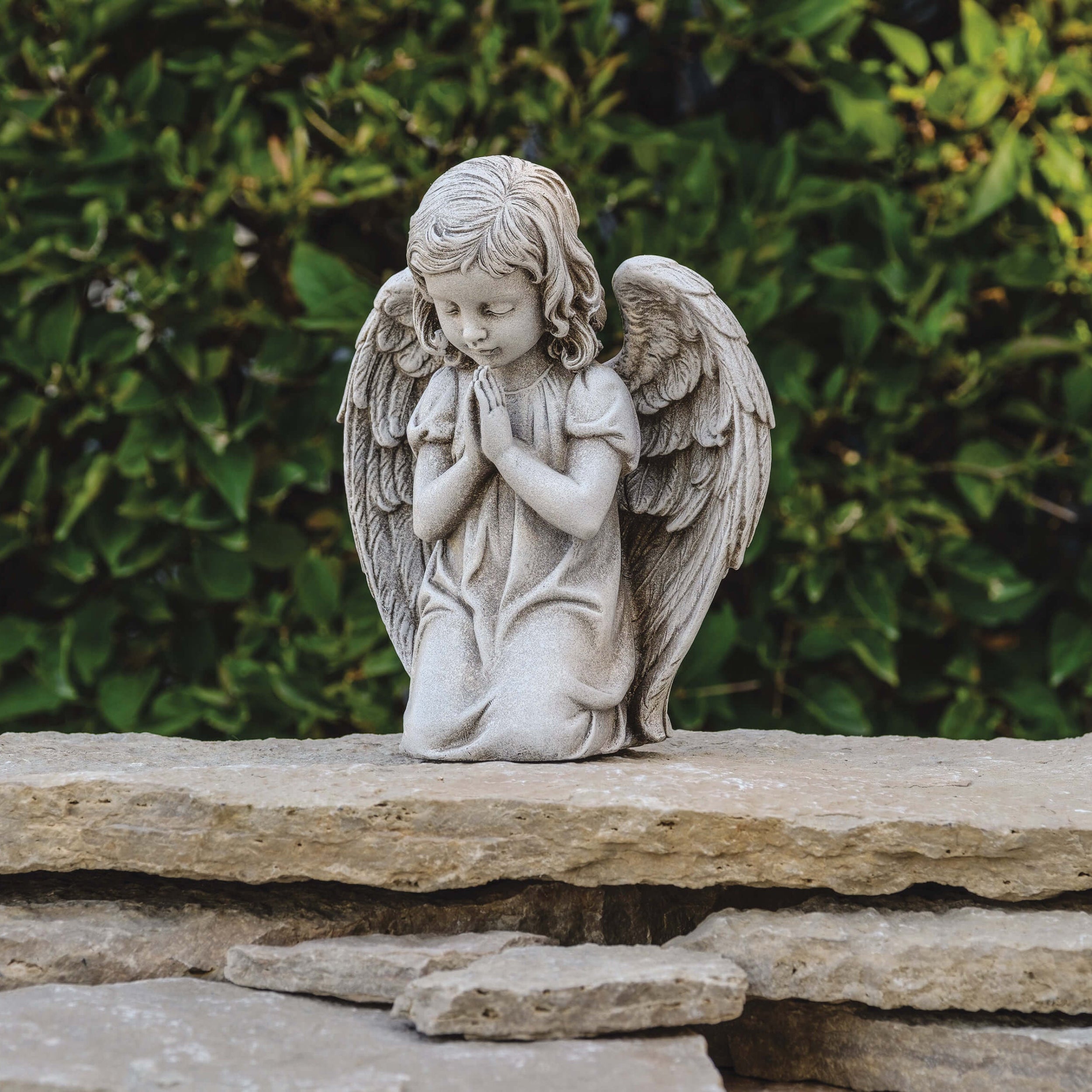 Stone angel statue on a rock with green foliage in the background