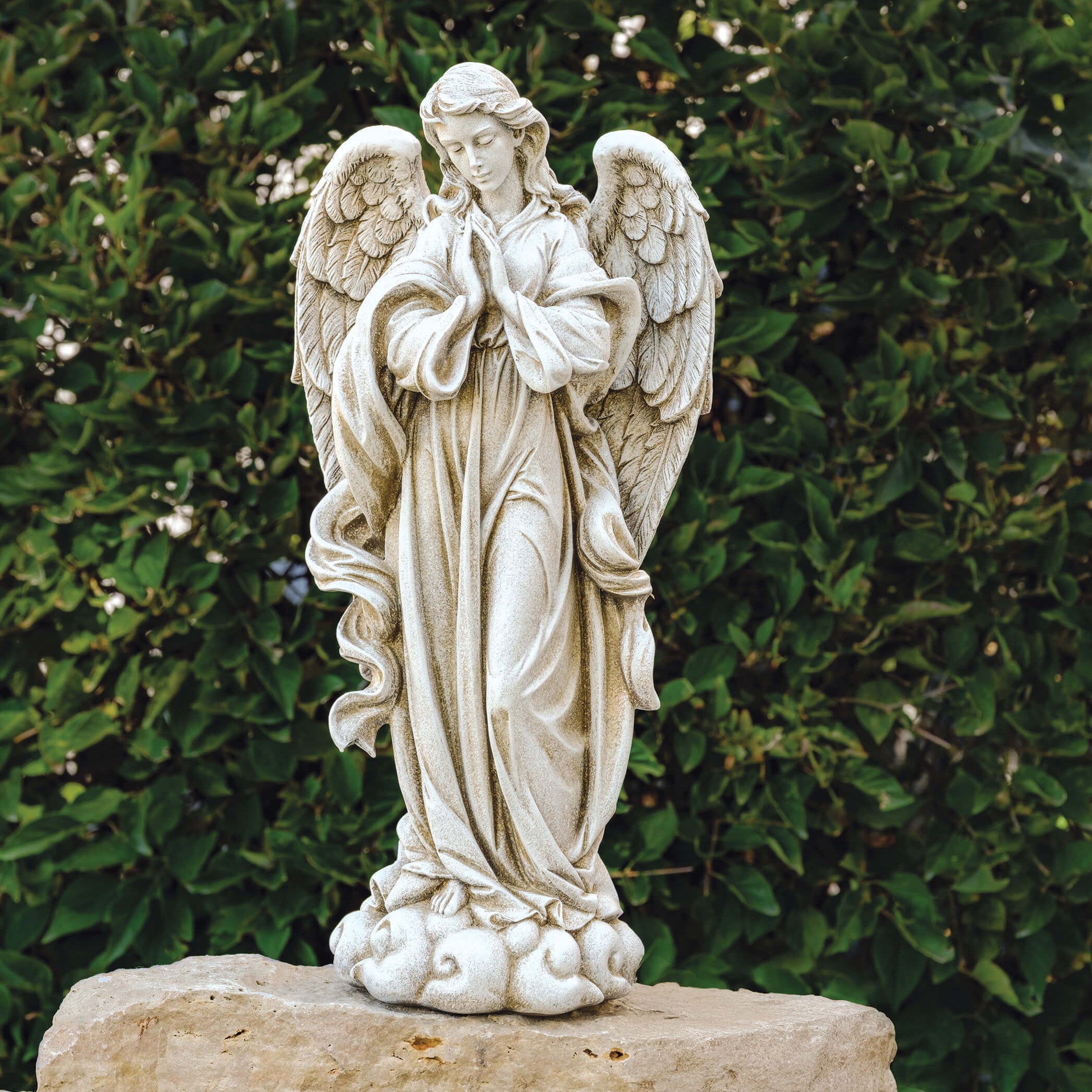 Statue of an angel on a stone pedestal against a green hedge background