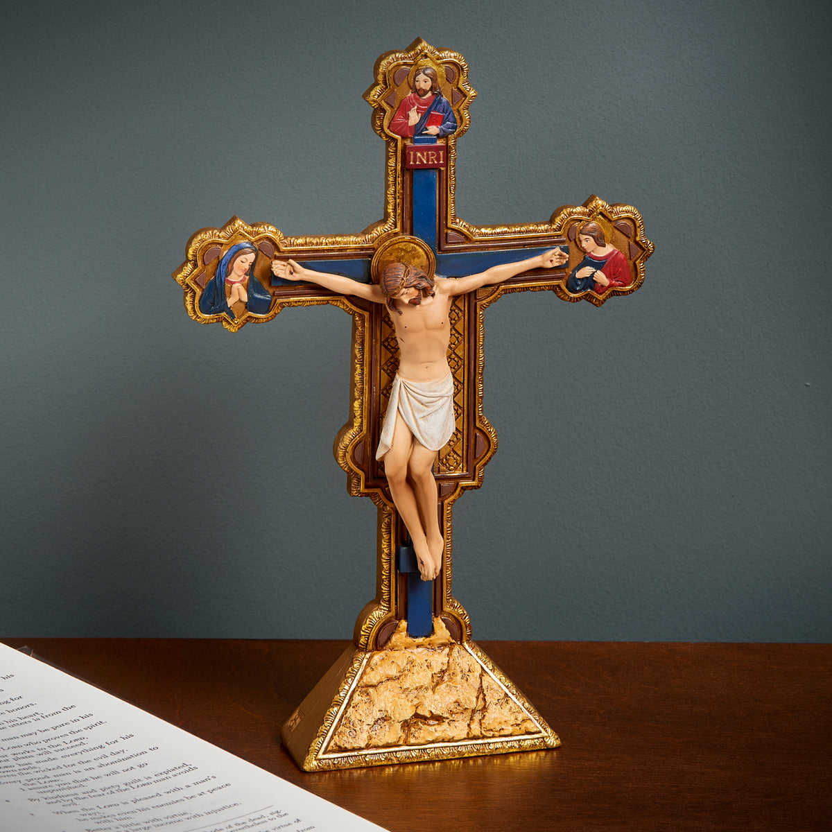 Joseph's Studio Ognissanti Tabletop Crucifix displayed on a tabletop against a dark background, showing the ornate cross and decorative base