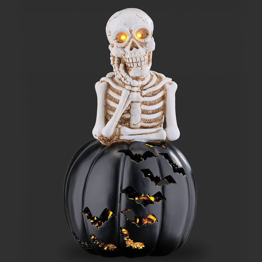 Skeleton figure on top of a black pumpkin with bat designs against a dark background