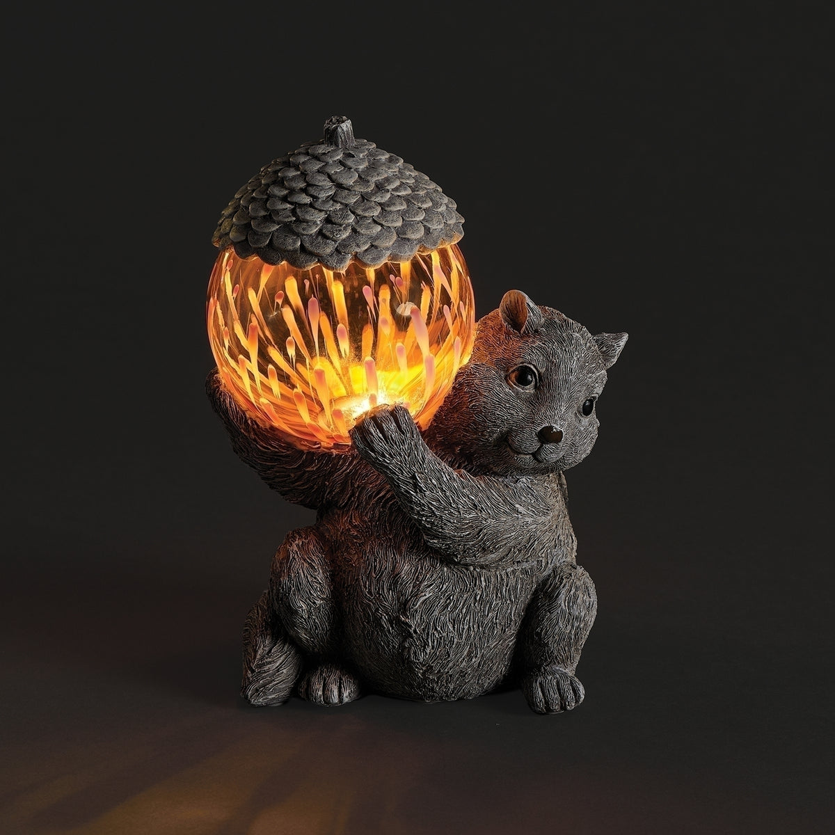 Pudgy Pals Solar-Powered Chipmunk Garden Statue illuminated at night with a warm glowing acorn