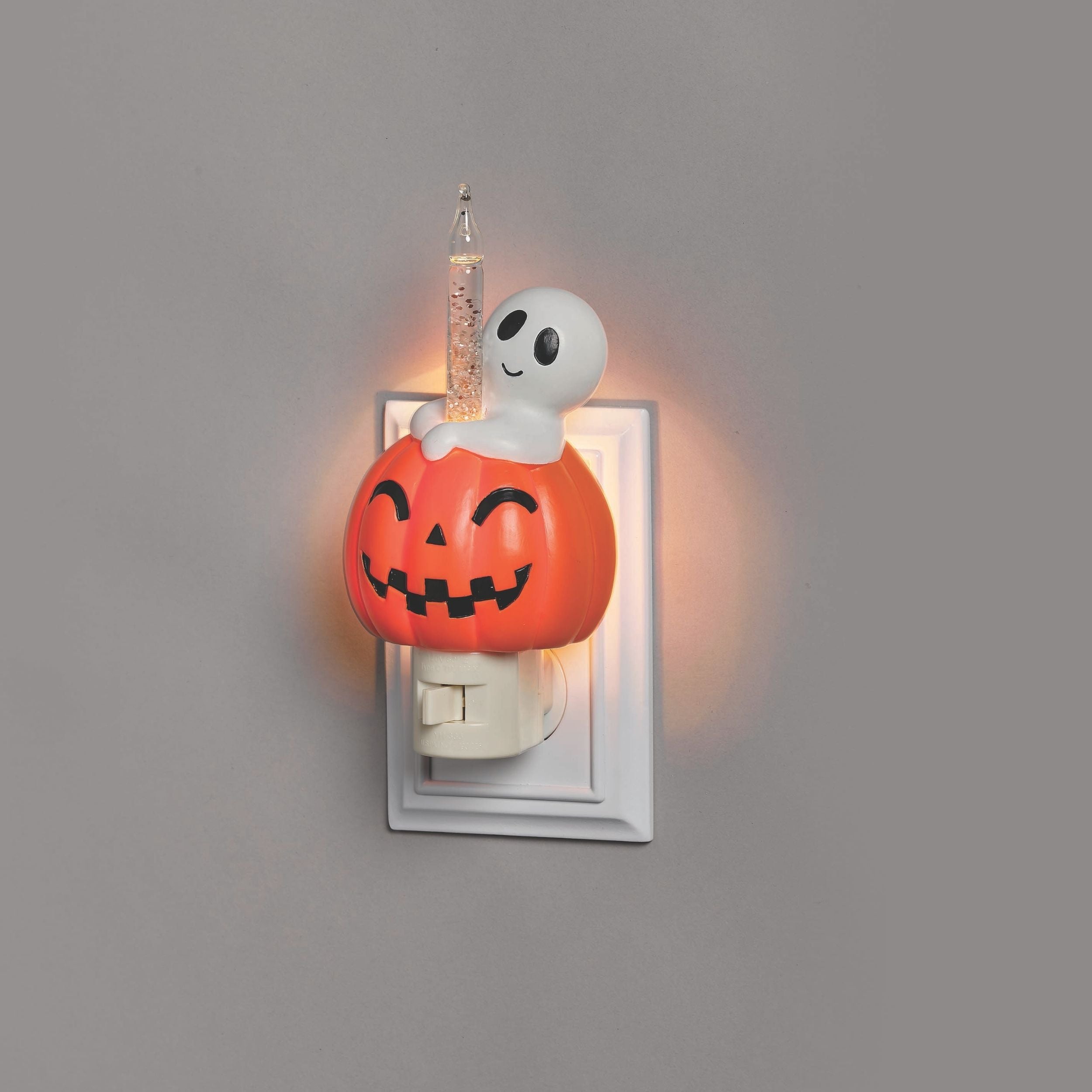 Halloween-themed night light with ghost and pumpkin design on a gray wall.