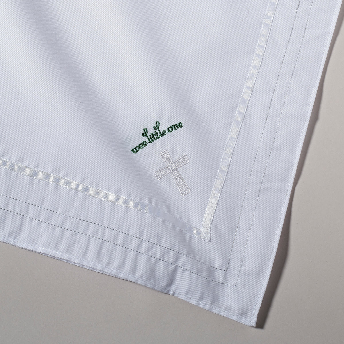 Close-up of white baptism baby blanket showing green shamrock embroidery and decorative stitched edging