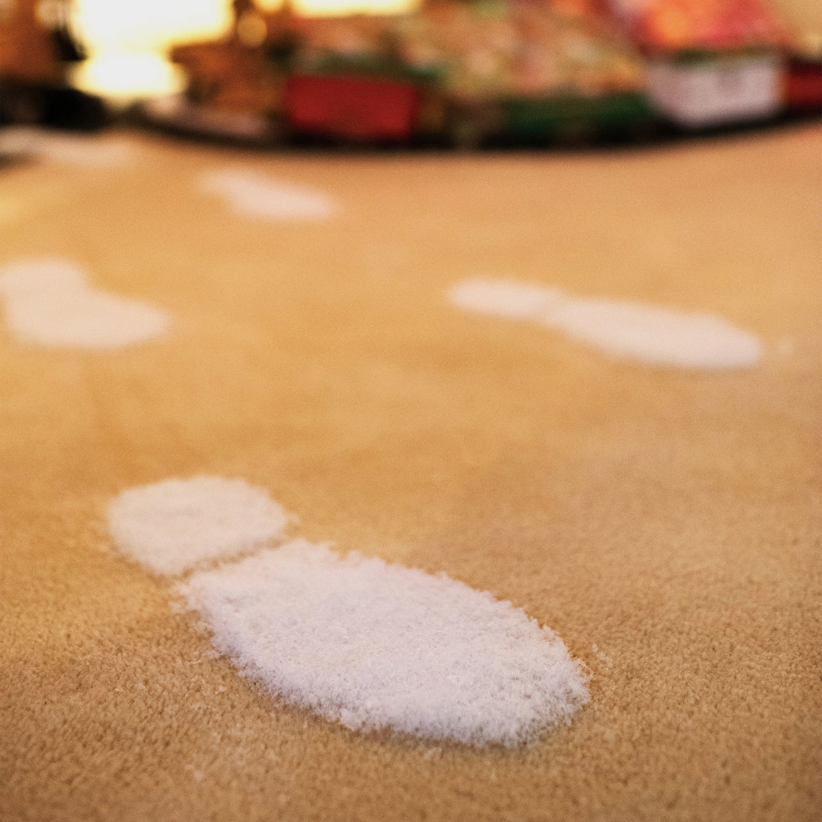 Close-up of artificial snow boot prints on a tan carpet, with a Christmas tree in the background.