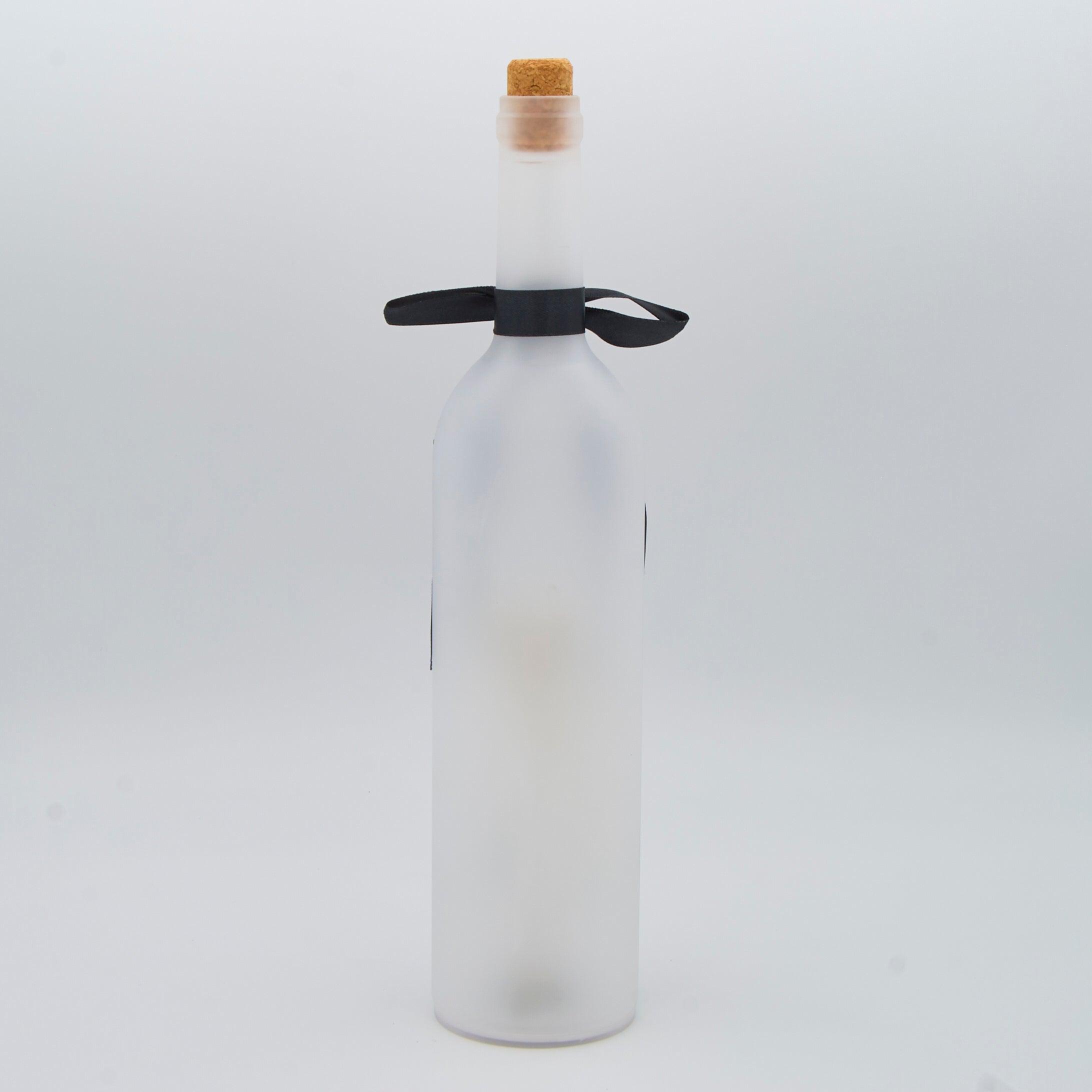 A frosted glass bottle with a cork stopper and a black ribbon tied around the neck, shown against a plain light gray background.
