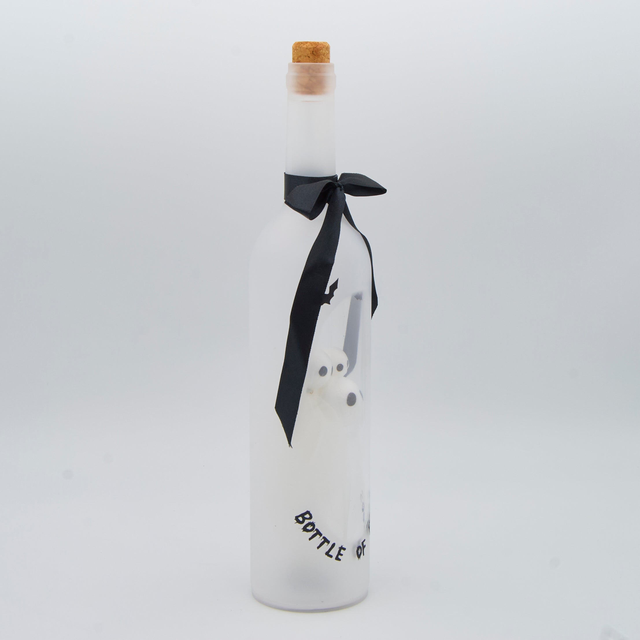A frosted glass bottle with a cork stopper, decorated with a black ribbon bow and a white ghost illustration, on a light gray background.