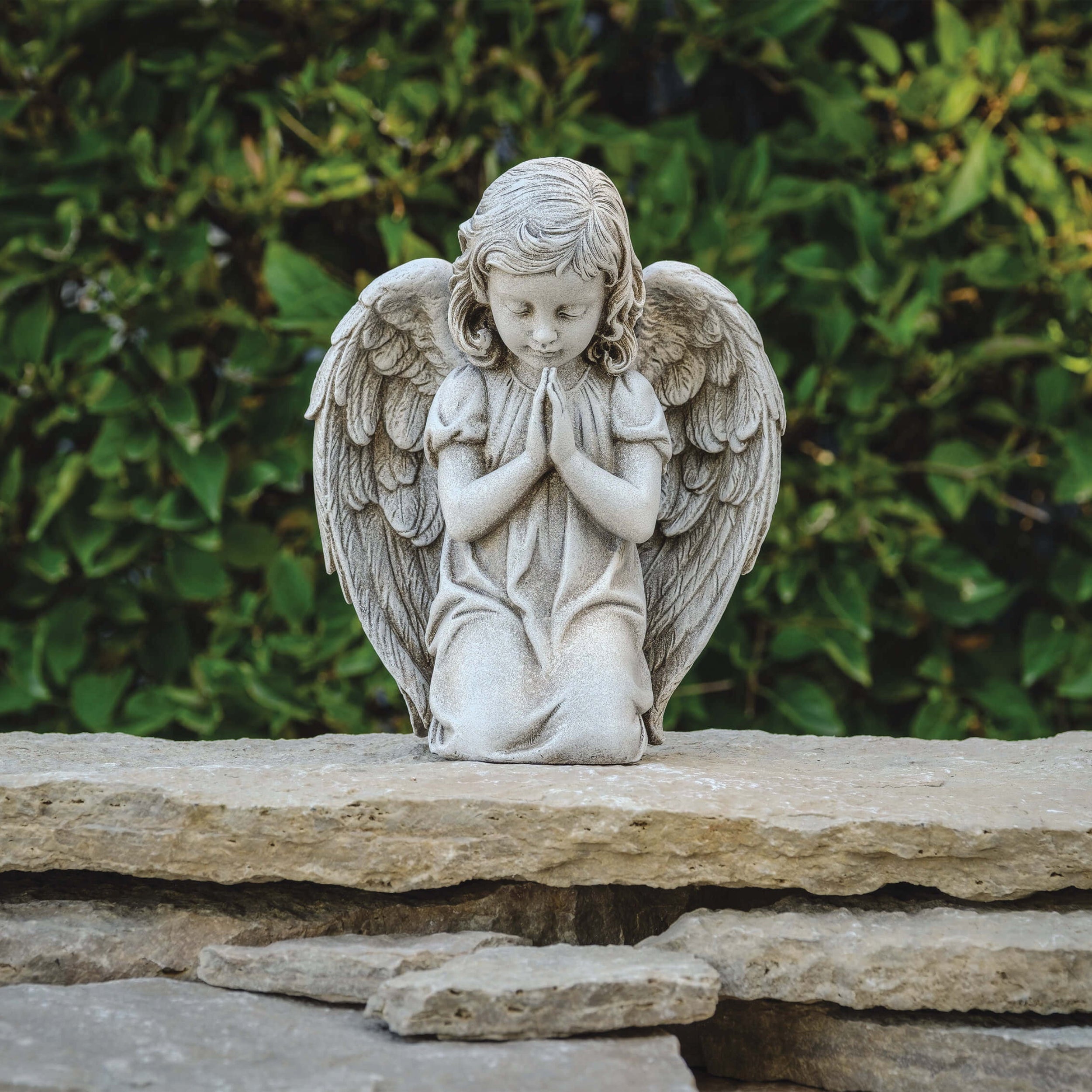 Stone angel statue on a rock with green foliage in the background