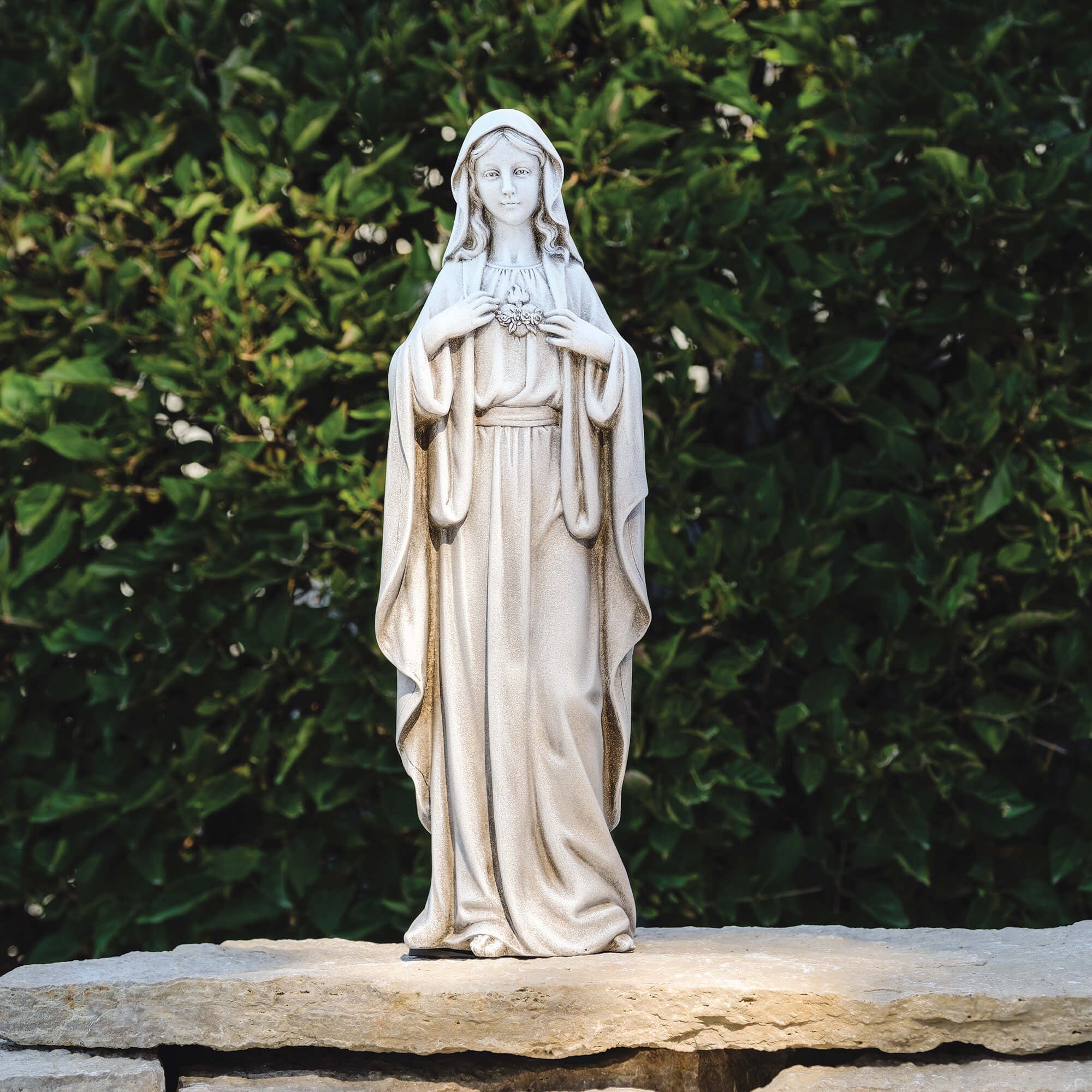 Statue of a religious figure on a stone platform with greenery in the background