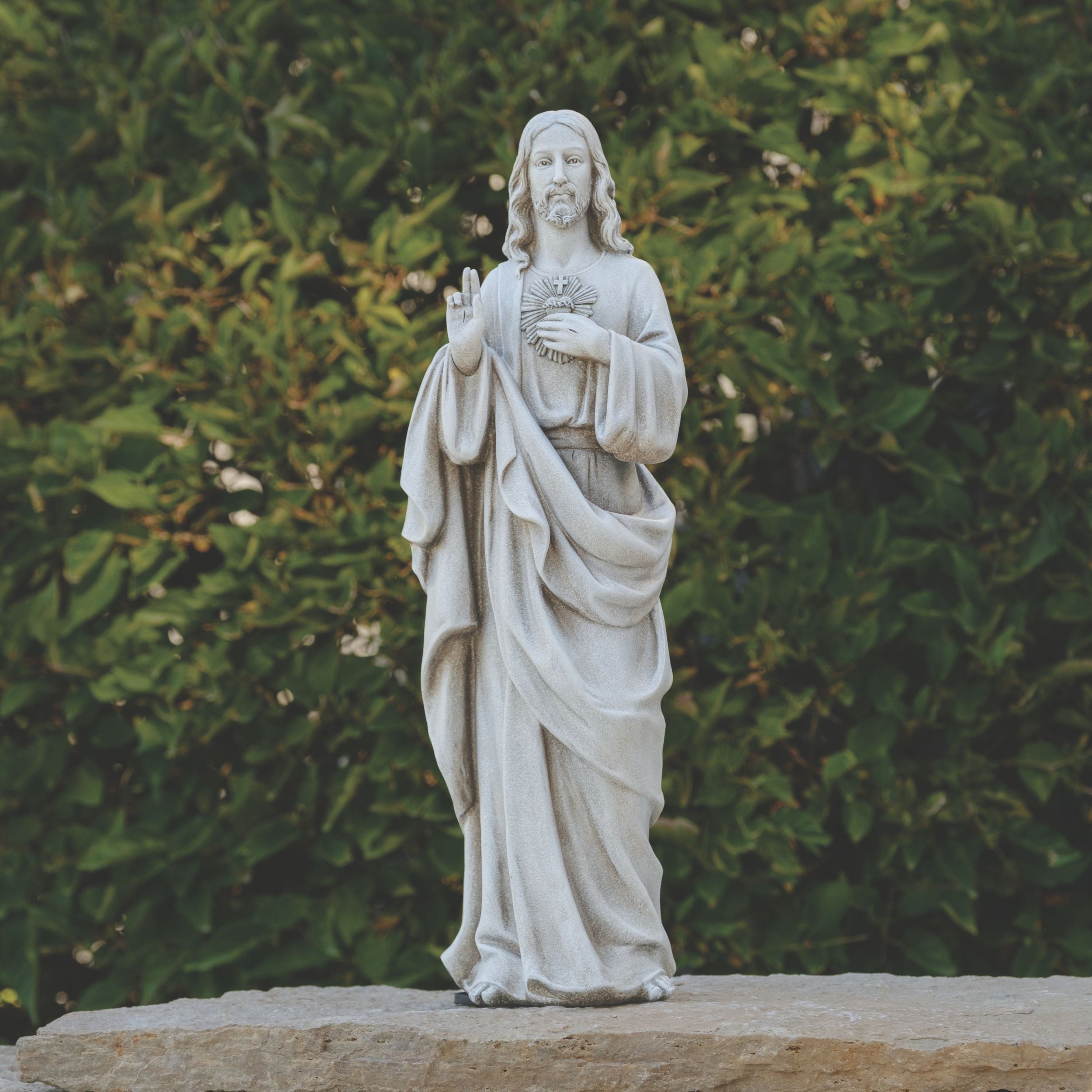 Statue of a religious figure in front of green foliage