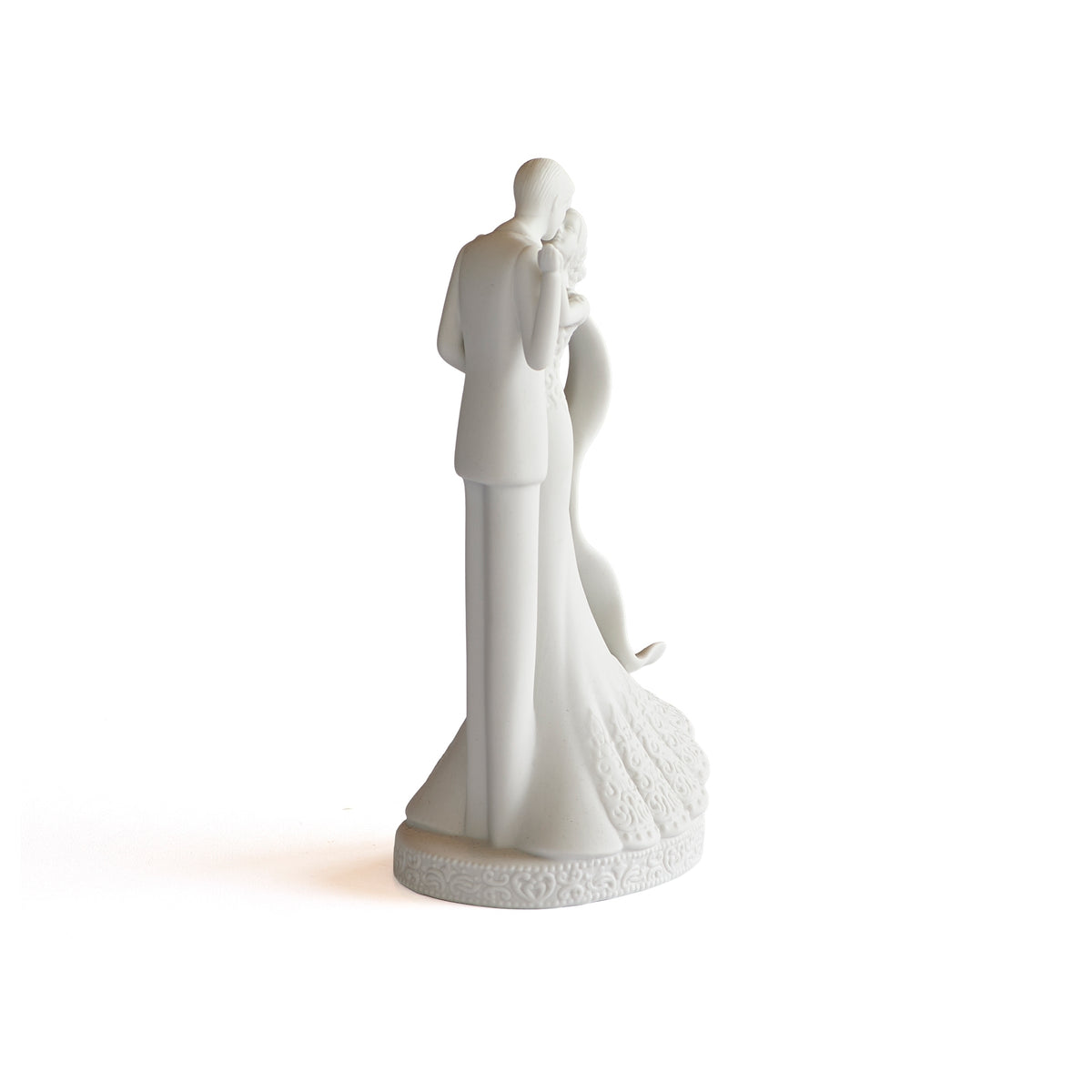 Angled rear view of white porcelain cake topper showing the couple’s embrace and gathered gown at the base.