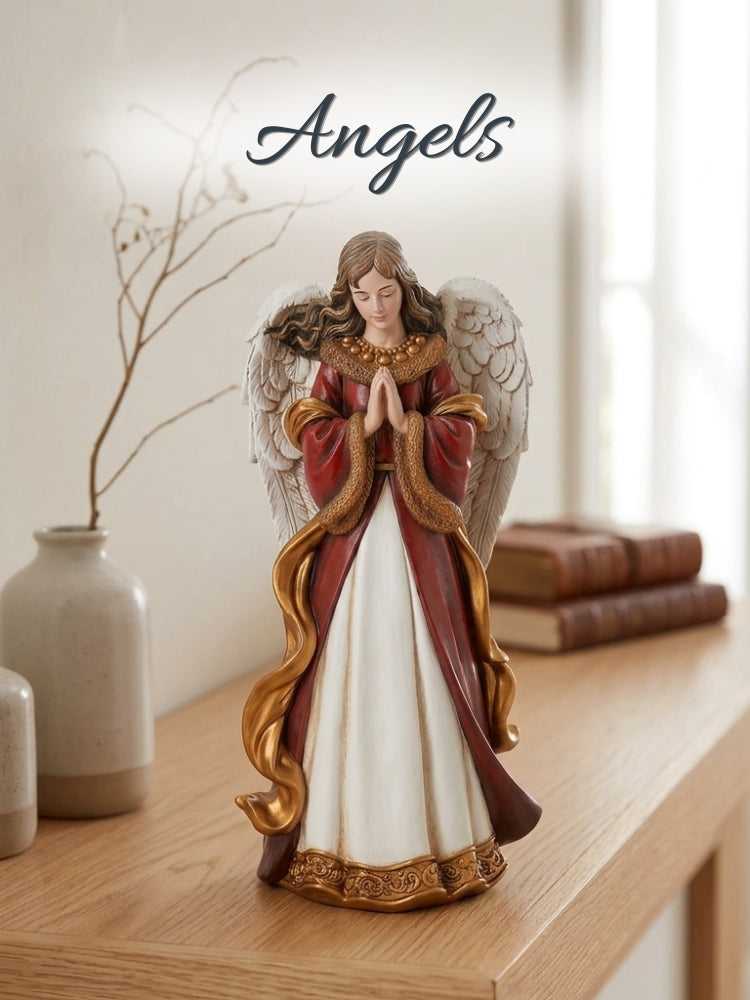 A praying angel figurine with white wings, a red and white gown, and gold trim, displayed on a wooden shelf next to a vase and books, with the word 'Angels' written above.