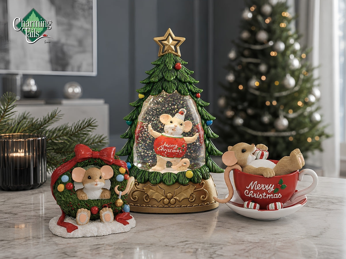 Three Christmas mouse figurines displayed on a marble surface in a decorated indoor setting: a central mouse inside a miniature tree with a gold star topper, a left mouse in a red holiday hat and green wreath, and a right mouse lounging in a red teacup saucer with candy stripes. A blurred Christmas tree and candle appear in the background.