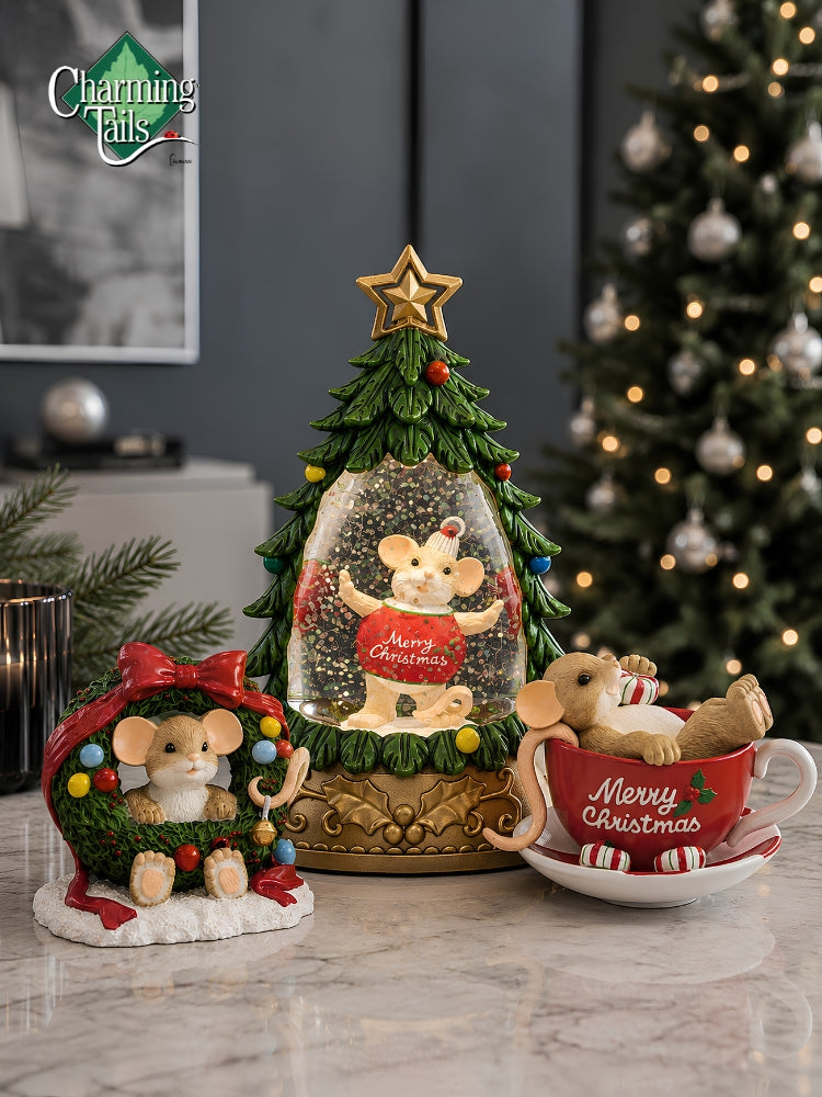 Three Christmas mouse-themed decorative products displayed on a marble surface: a tree-shaped snow globe with a mouse inside, a wreath-shaped mouse figurine with a red bow, and a red teacup-shaped mouse figure with a plush mouse. A blurred Christmas tree and indoor room background are visible.