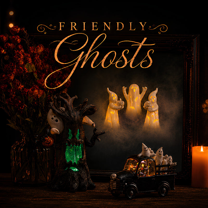 Halloween-themed decorative scene with a framed display reading 'Friendly Ghosts' in gold lettering. The frame shows glowing cream ghost figures, a dark tree stump with green lights, a small black toy truck carrying white ghosts, dried red flowers, and a lit candle on a wooden surface.