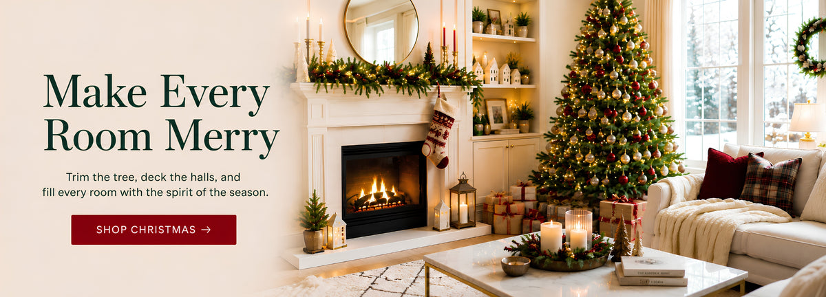 A festive holiday living room scene with a decorated Christmas tree, fireplace, mantel garland, candles, wrapped gifts, and a sofa. Large text on the left reads 'Make Every Room Merry' with a red 'SHOP CHRISTMAS' button.