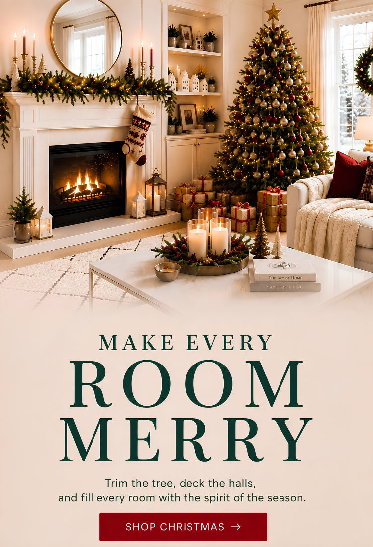 A festive Christmas living room scene with a decorated tree, fireplace, candles, and wrapped gifts, overlaid with the text 'MAKE EVERY ROOM MERRY' and a red 'SHOP CHRISTMAS ->' button.